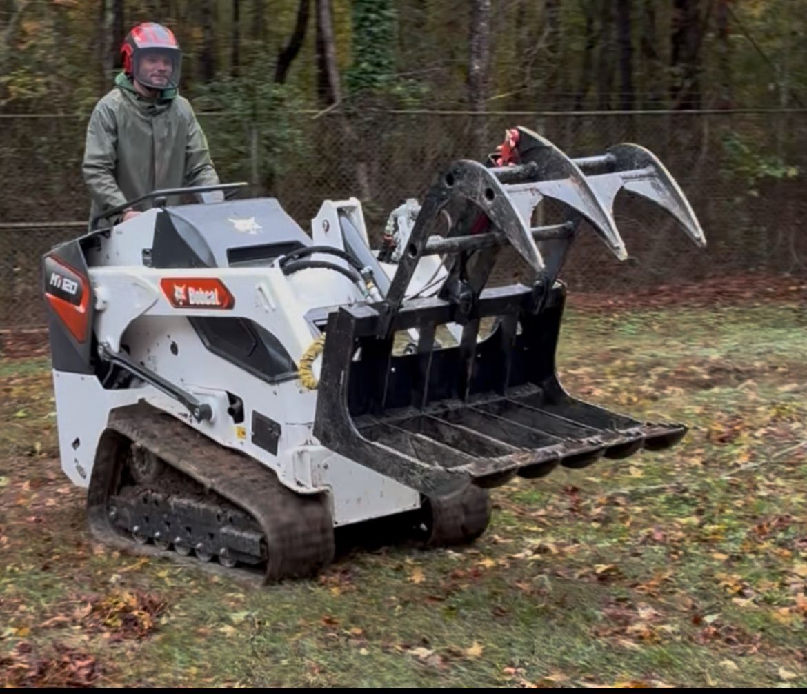 Person operating a Bobcat compact track loader with grapple attachment in an outdoor setting.