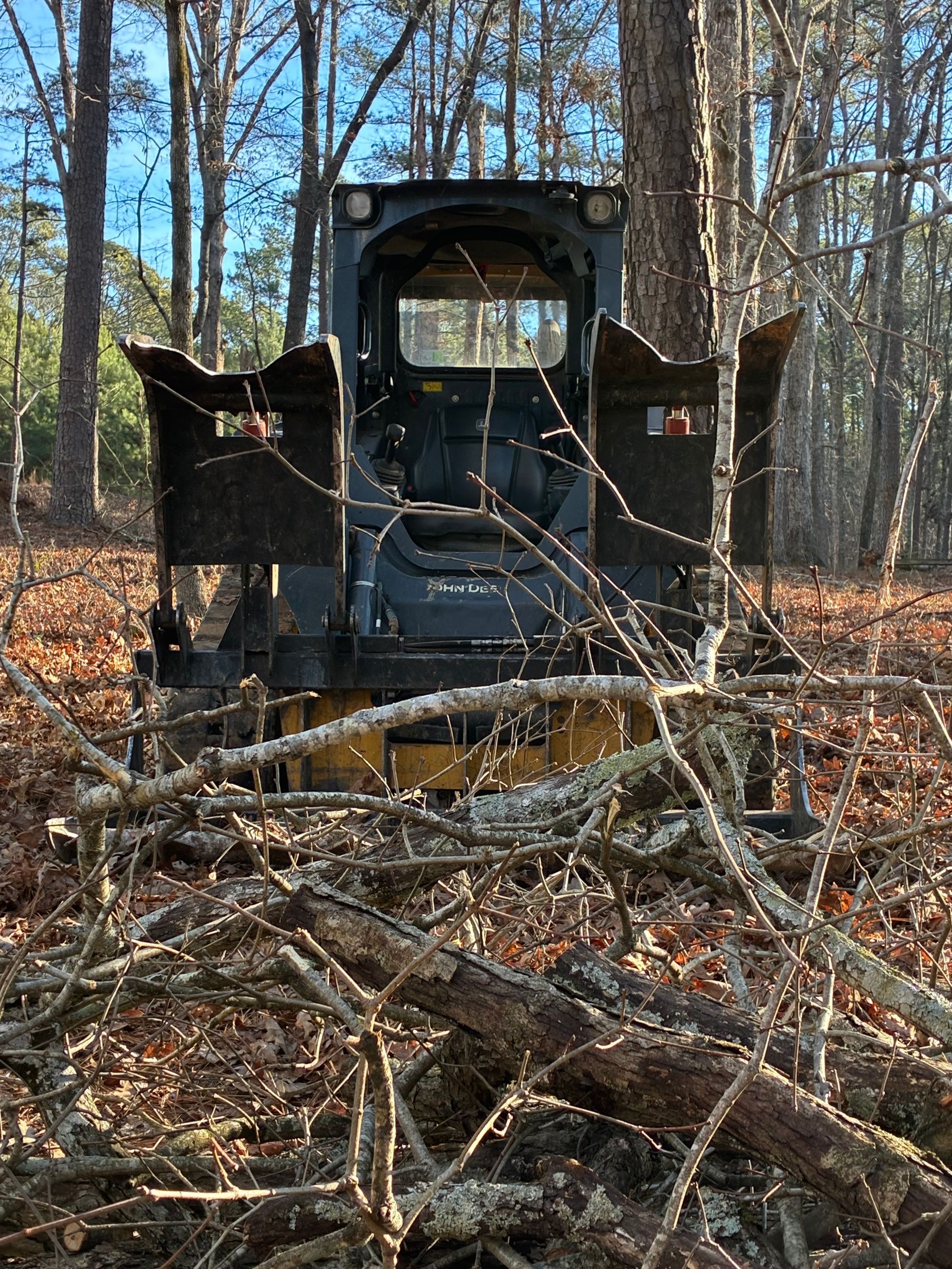 Small, black construction vehicle in a wooded area, surrounded by branches.