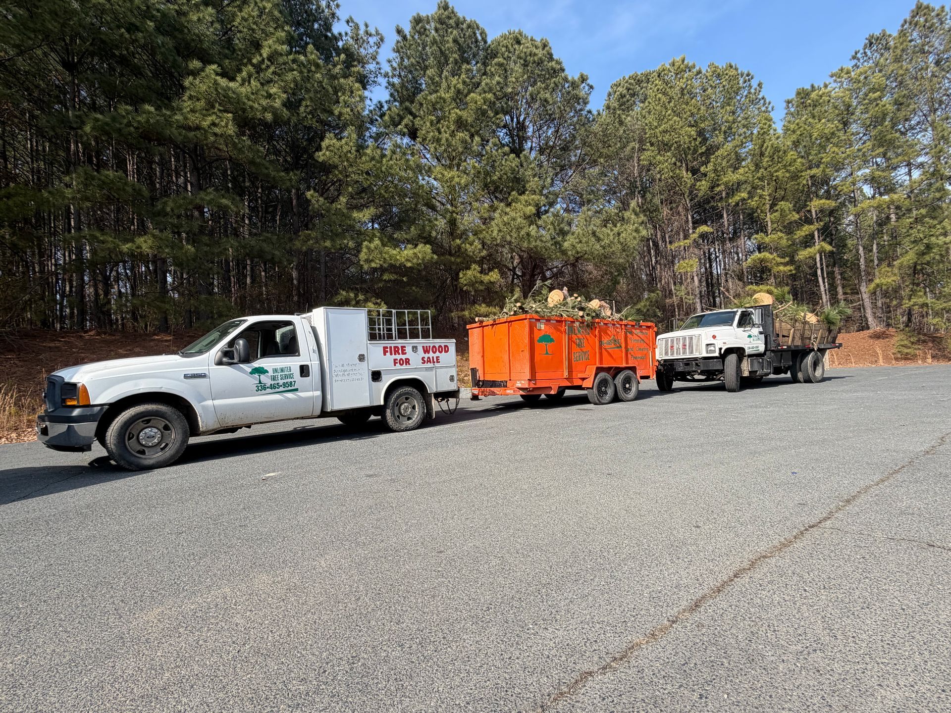 White work trucks and orange trailer loaded with wood debris parked outdoors.