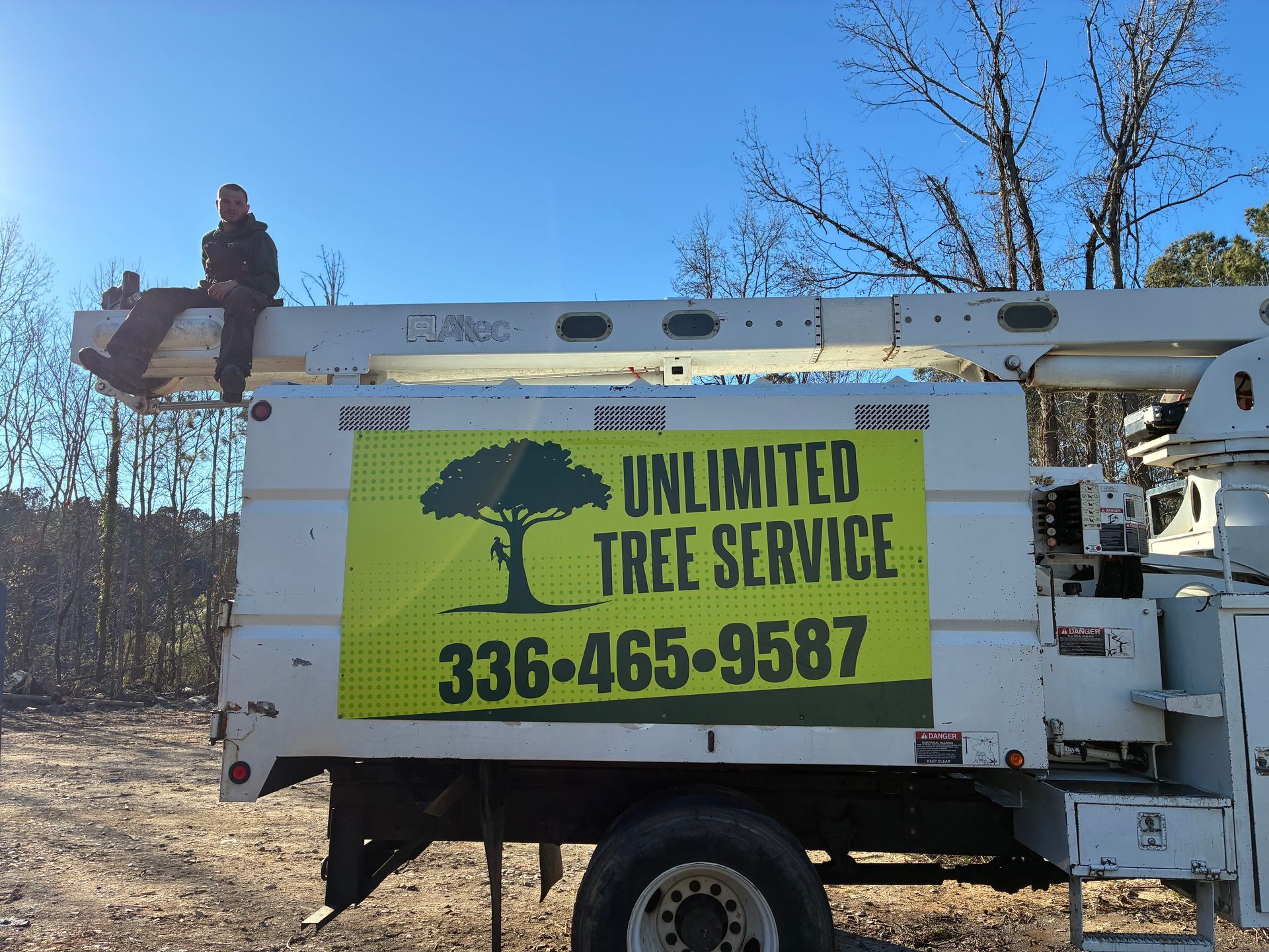 A tree service truck with a man sitting in the bucket, sunny day. 
