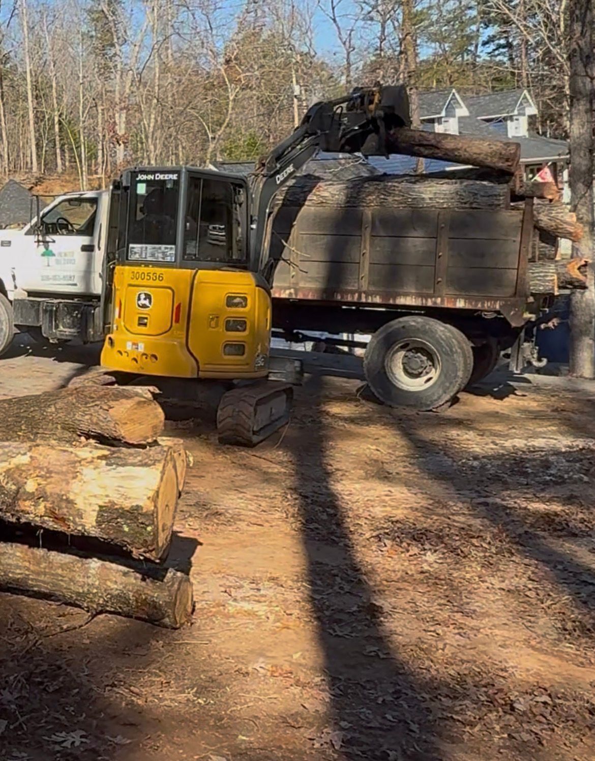 A yellow excavator loading logs into a truck on a sunny day.