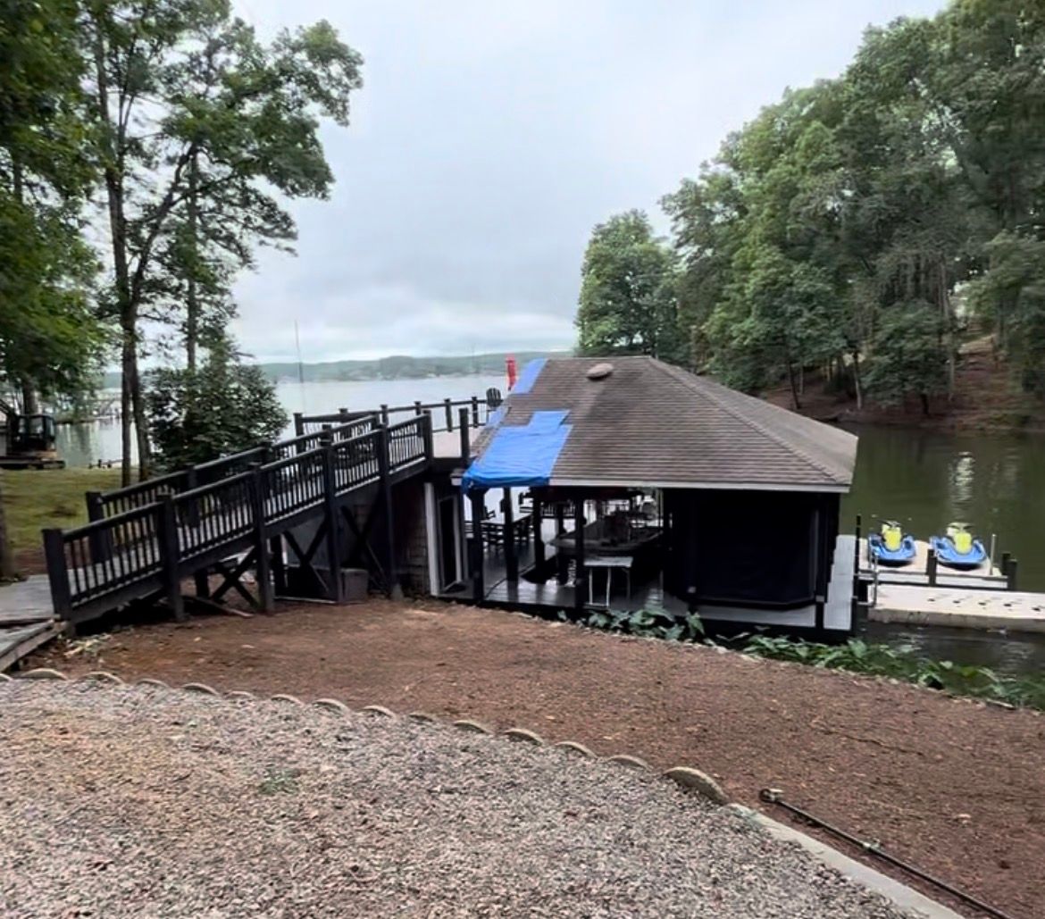 Boathouse on lake with ramp and dock. Black structure with dark roof, blue tarp, and two yellow kayaks.