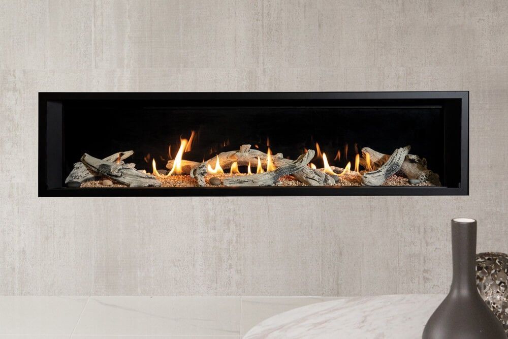 Modern linear gas fireplace with flames and logs set into a gray wall, with a vase on a light surface