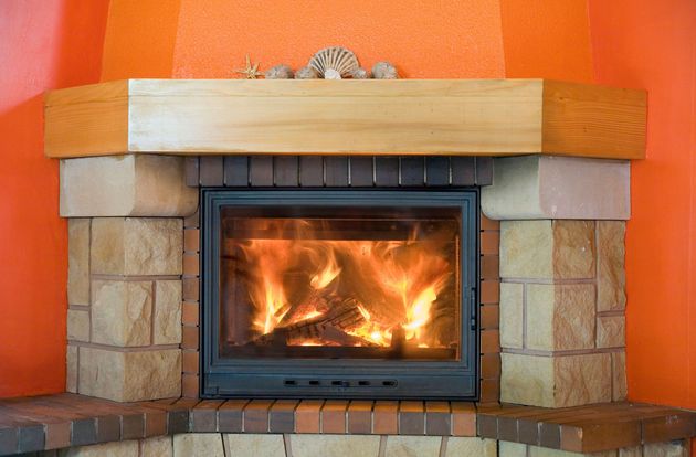 A cozy fireplace with a burning fire, surrounded by stone masonry and an orange wall, featuring a wood mantel above.