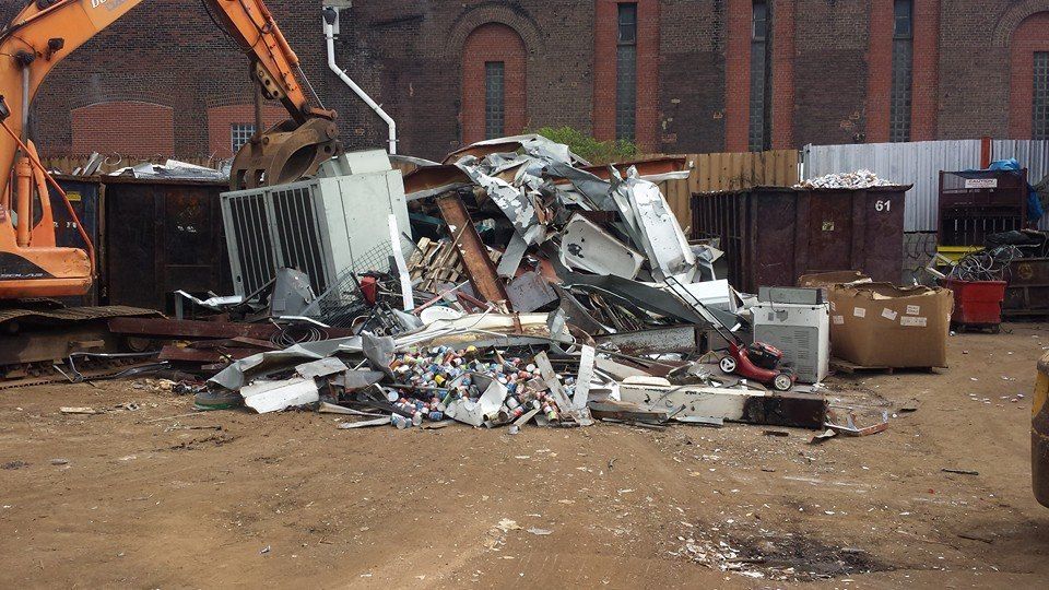 Pile of crushed scrap metal and debris in an industrial yard beside a brick building