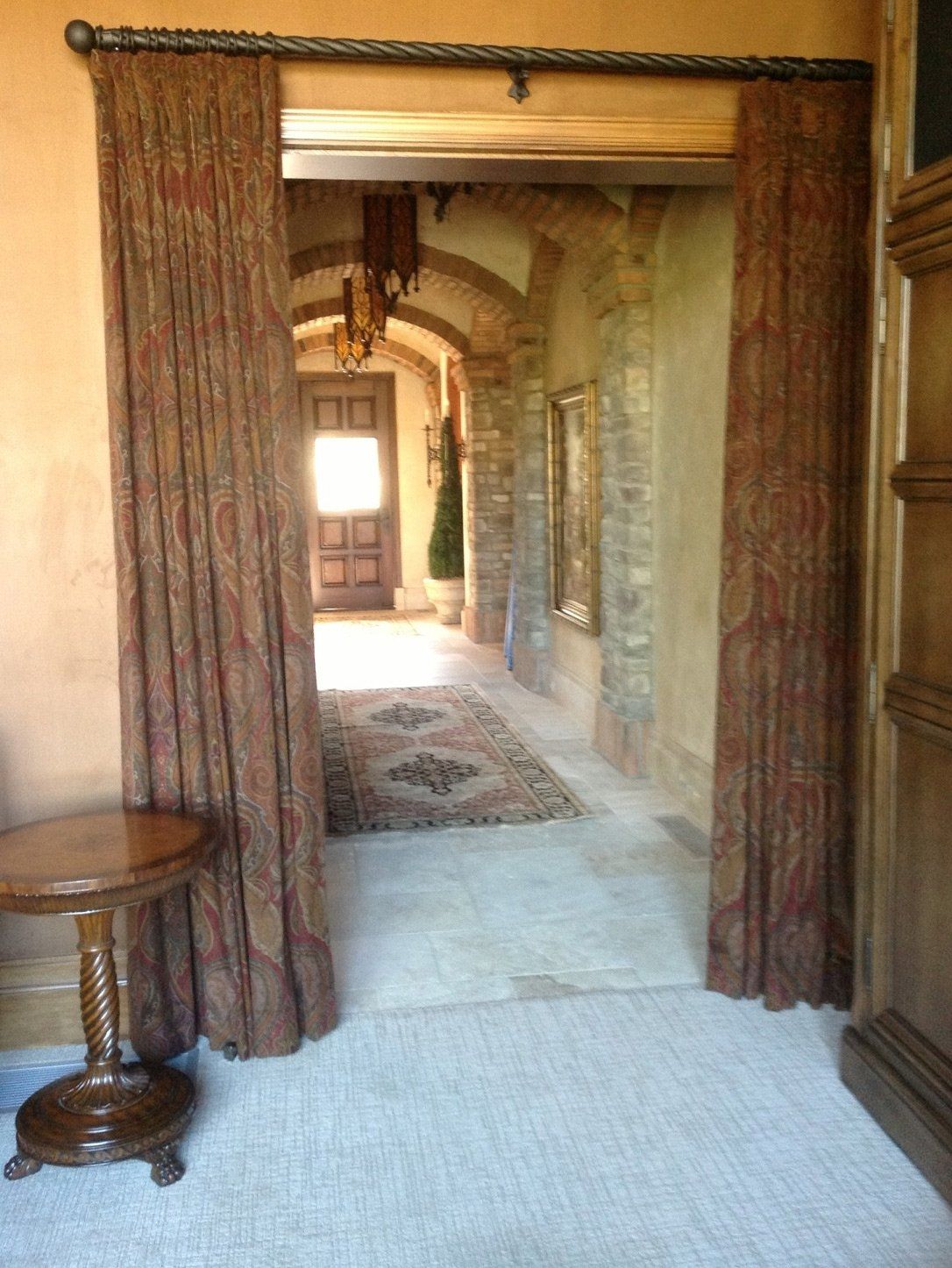 A hallway with a table and curtains leading to a door.