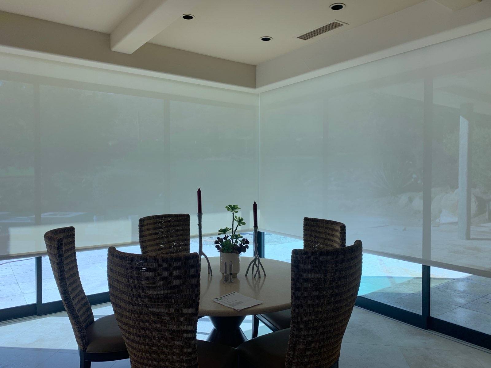 A dining room with a table and chairs and blinds on the windows.