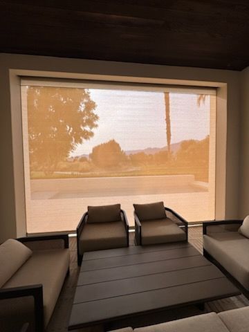 Interior with seating, window shade, and a view of landscape under a beige hue.