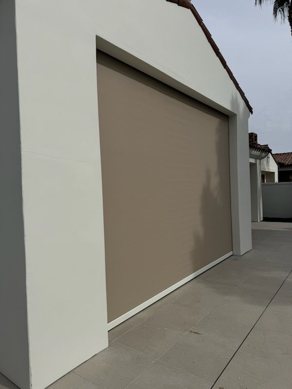 Beige shade covering a garage opening, set in white stucco wall.