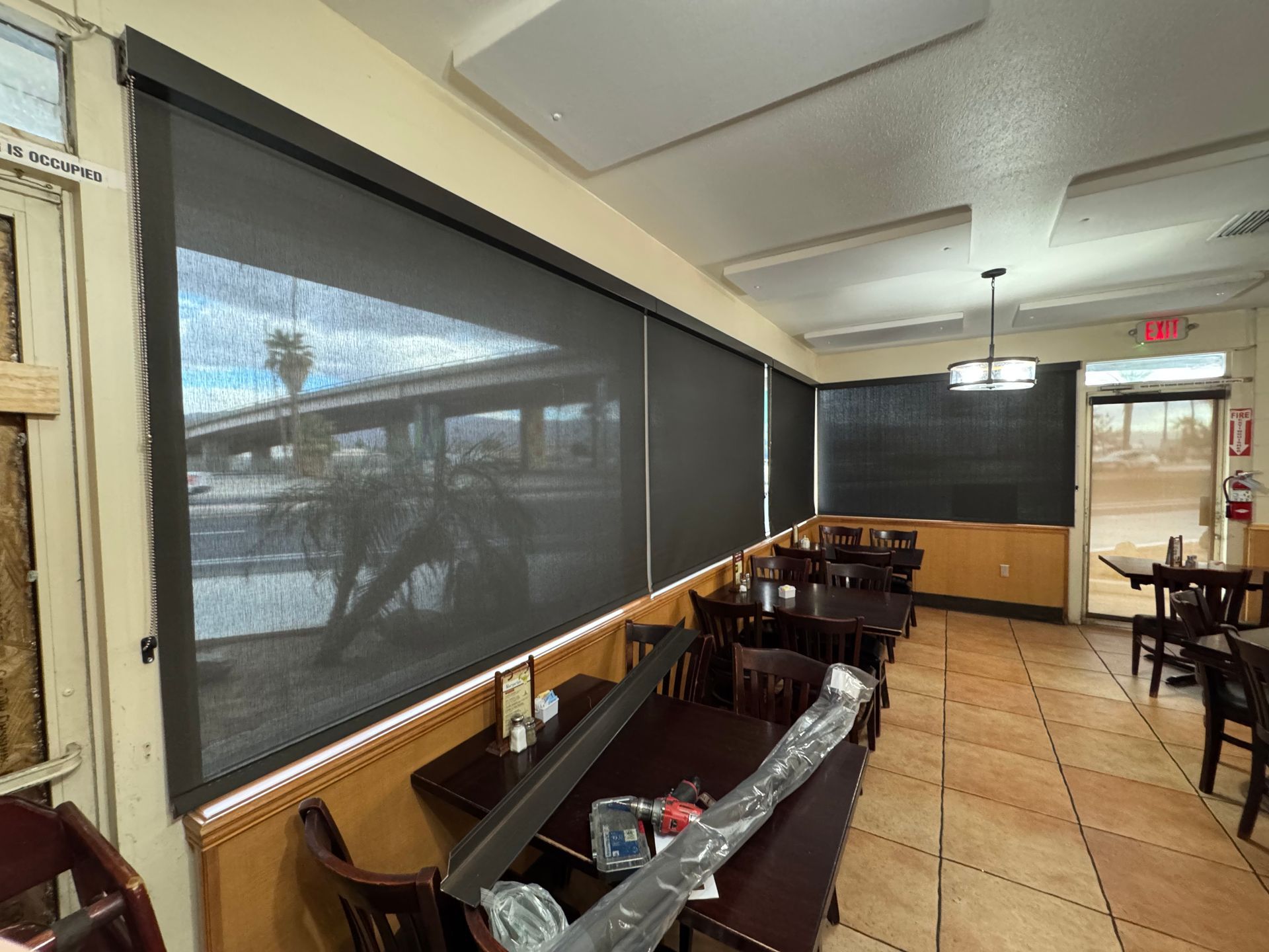 A restaurant with tables and chairs and a large window with blinds.