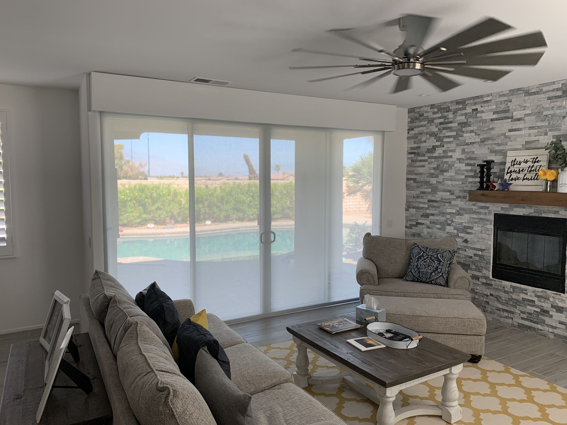 Living room with a pool view, featuring a couch, arm chair, fireplace, and large windows with shades.
