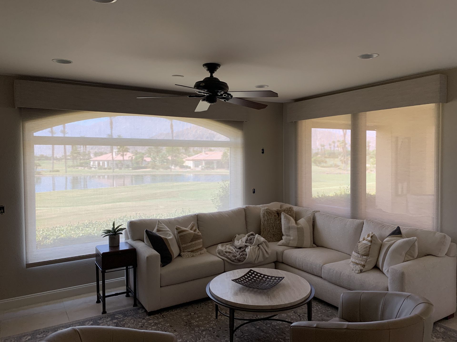 Living room with a white sectional sofa, round coffee table, and view of a lake through a large window.