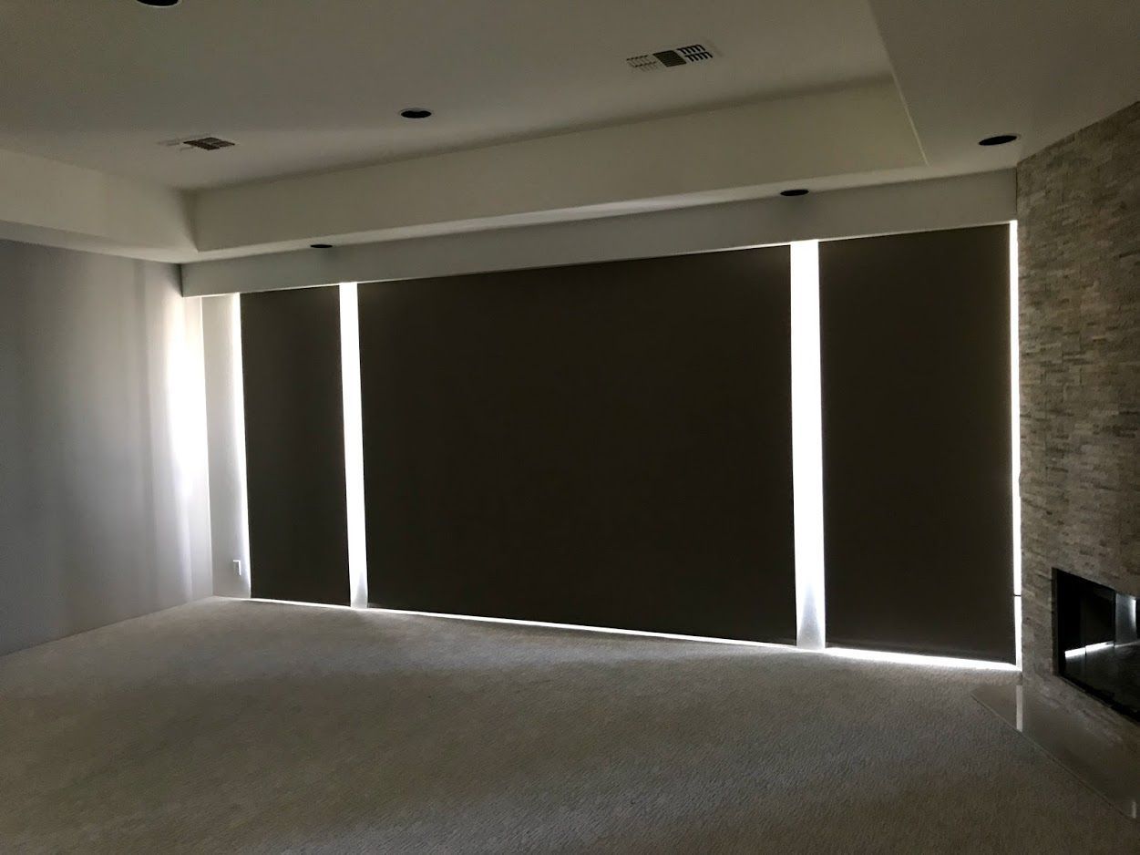 Room with dark roller shades, recessed lighting, and a stone fireplace. Sunlight peeks through gaps in the shades.
