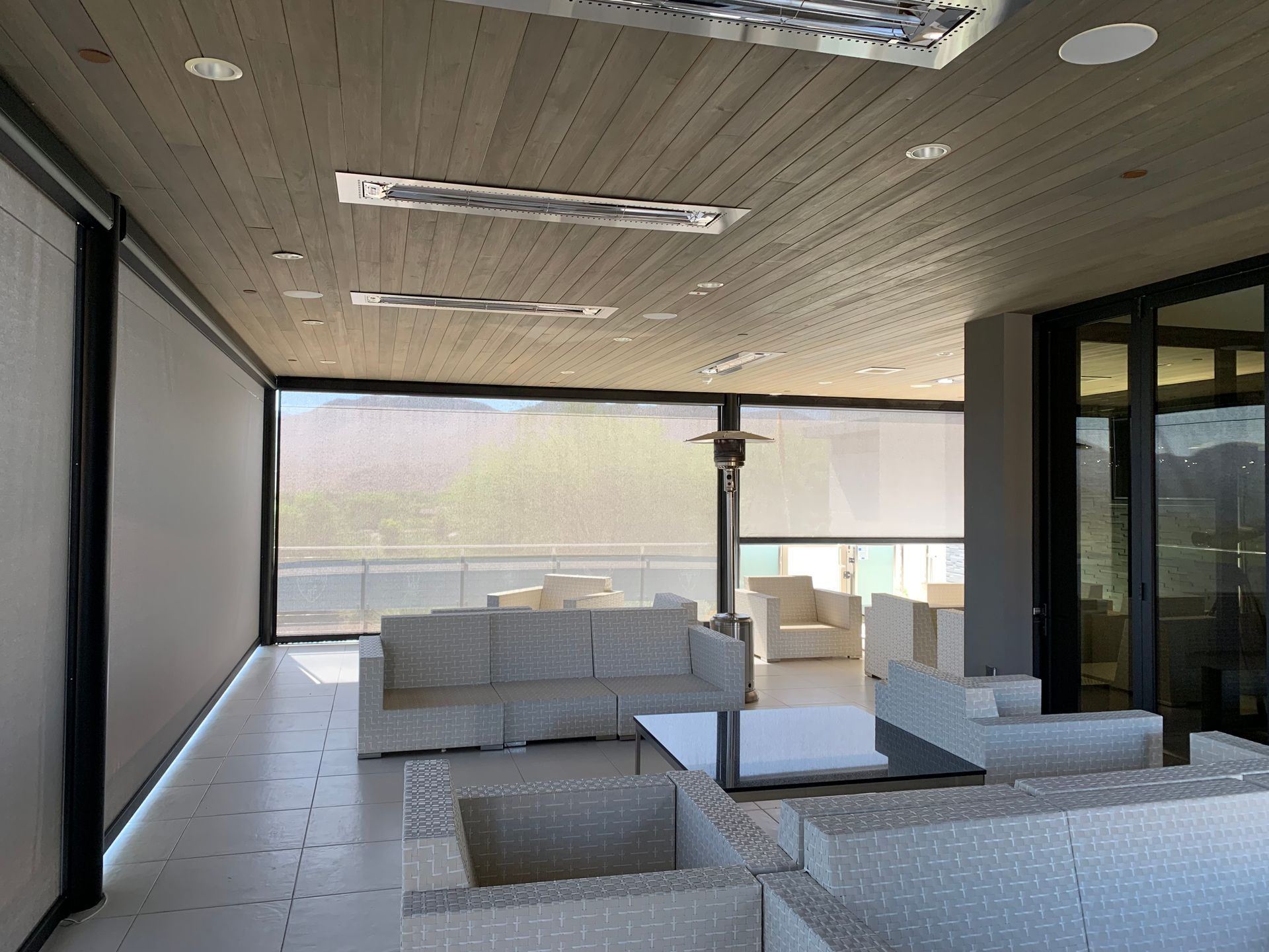 Outdoor seating area with white wicker furniture, retractable shades, and wood ceiling.
