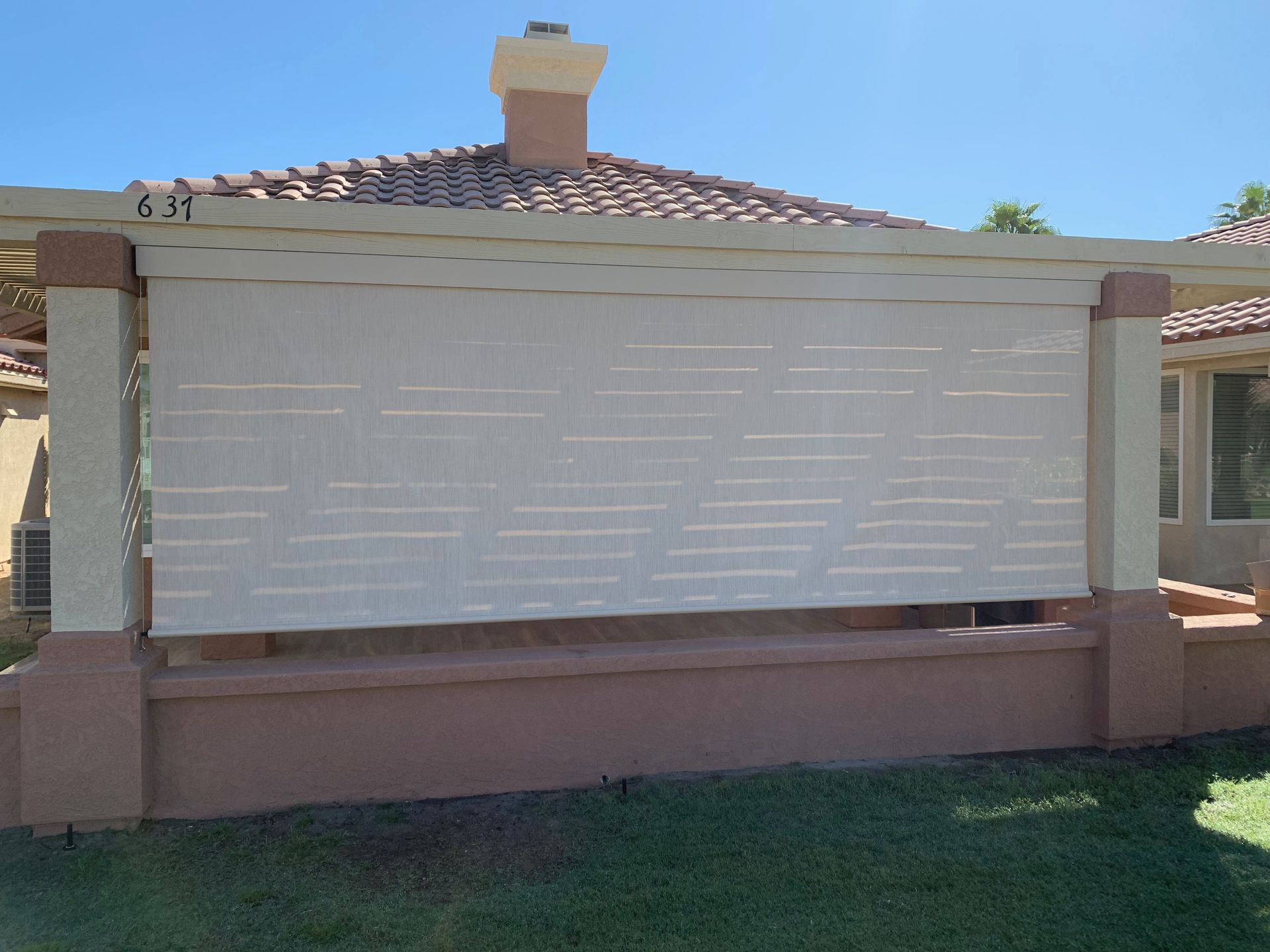 Beige exterior sun shade on a tan-colored house with green grass and blue sky.