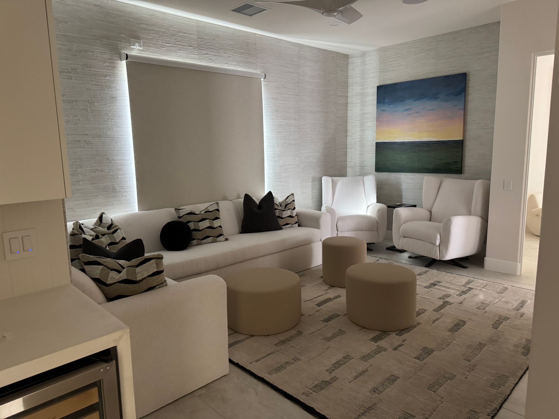 A living room with a couch , chairs , ottomans and a painting on the wall.