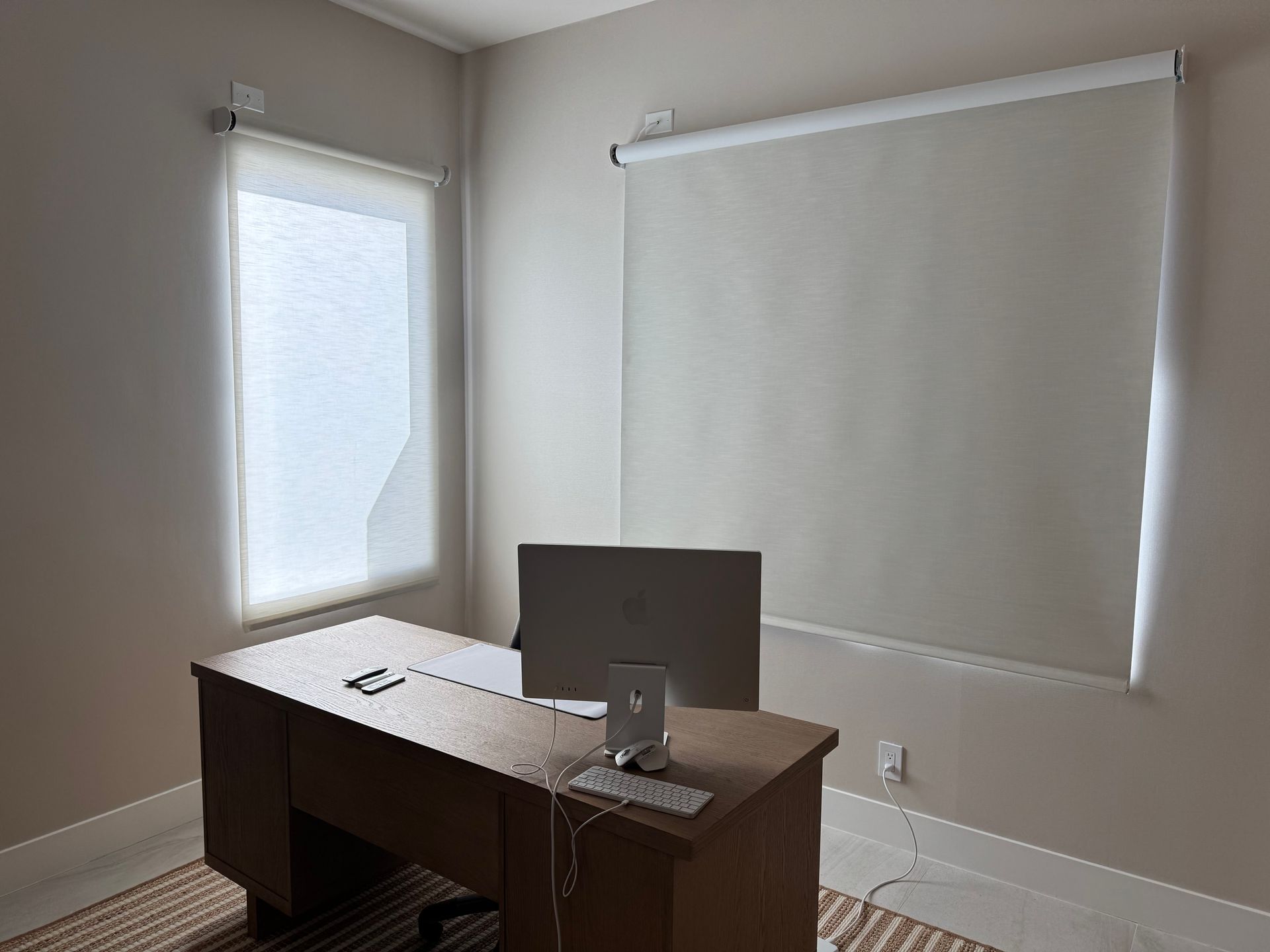 A desk with a computer on it in a room with a projector screen on the wall.