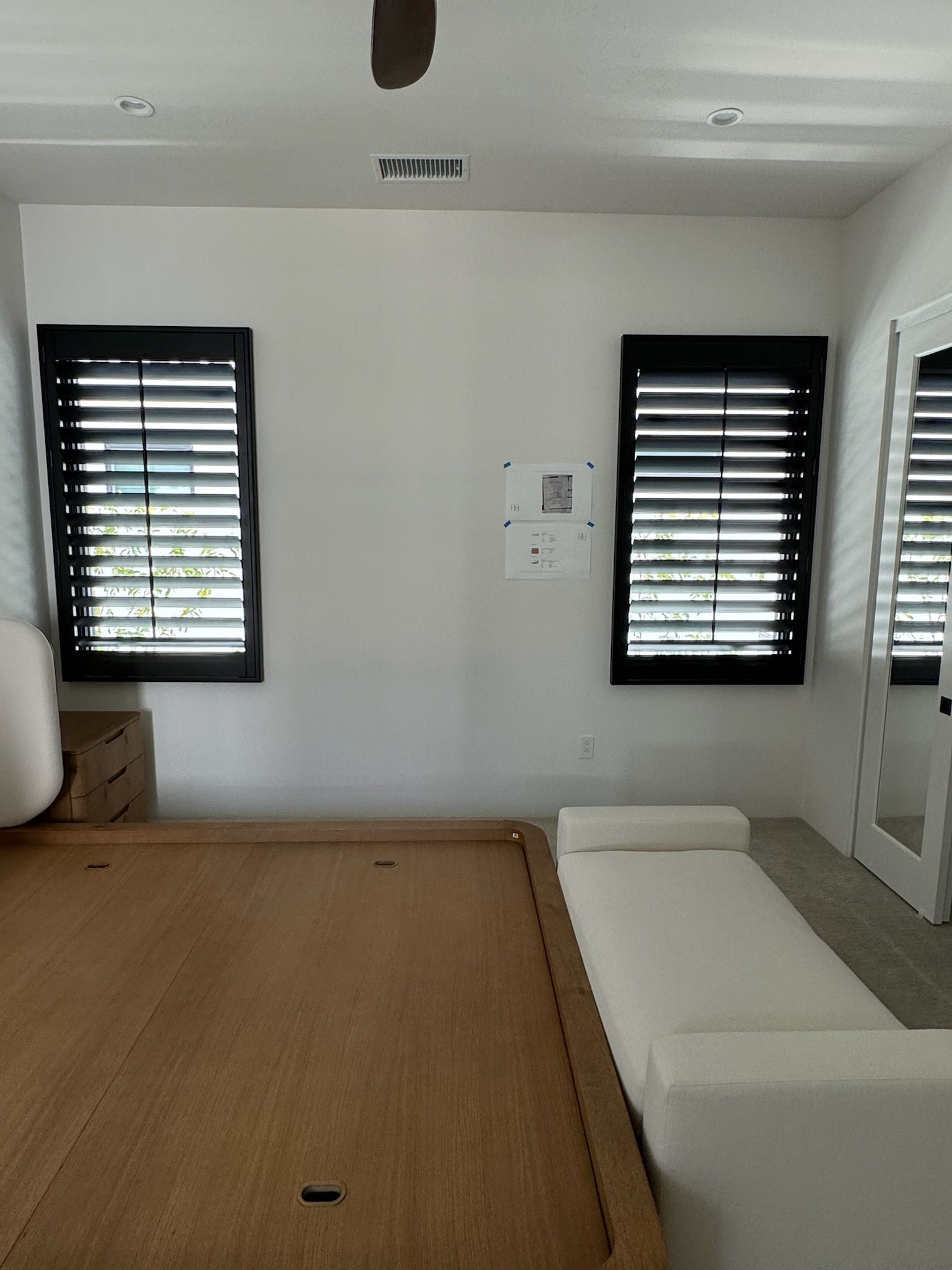 A bedroom with a bed, a couch, a mirror, and shutters on the windows.