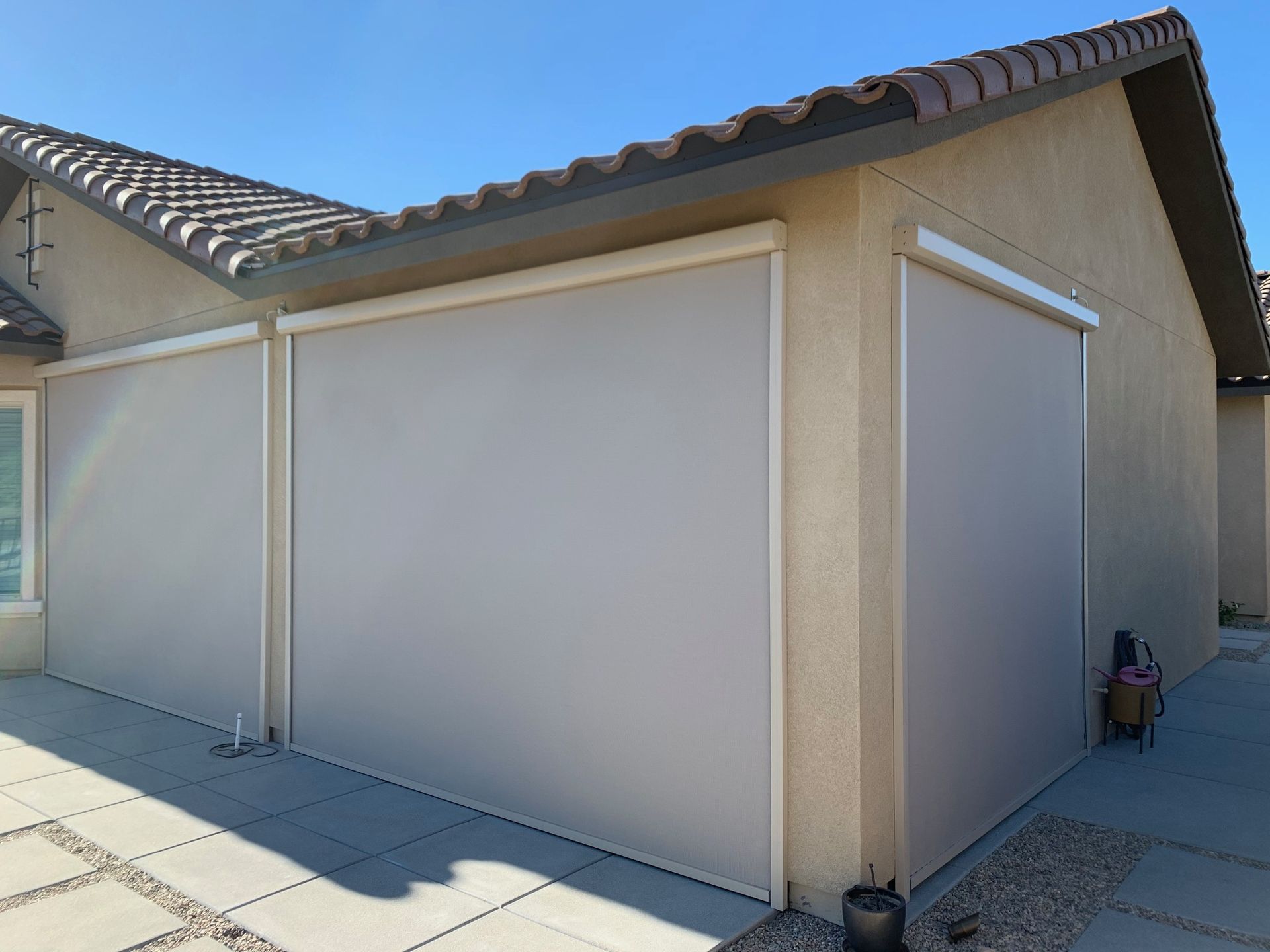Beige retractable sun shades on a tan building's exterior, blocking sunlight. Paved patio.