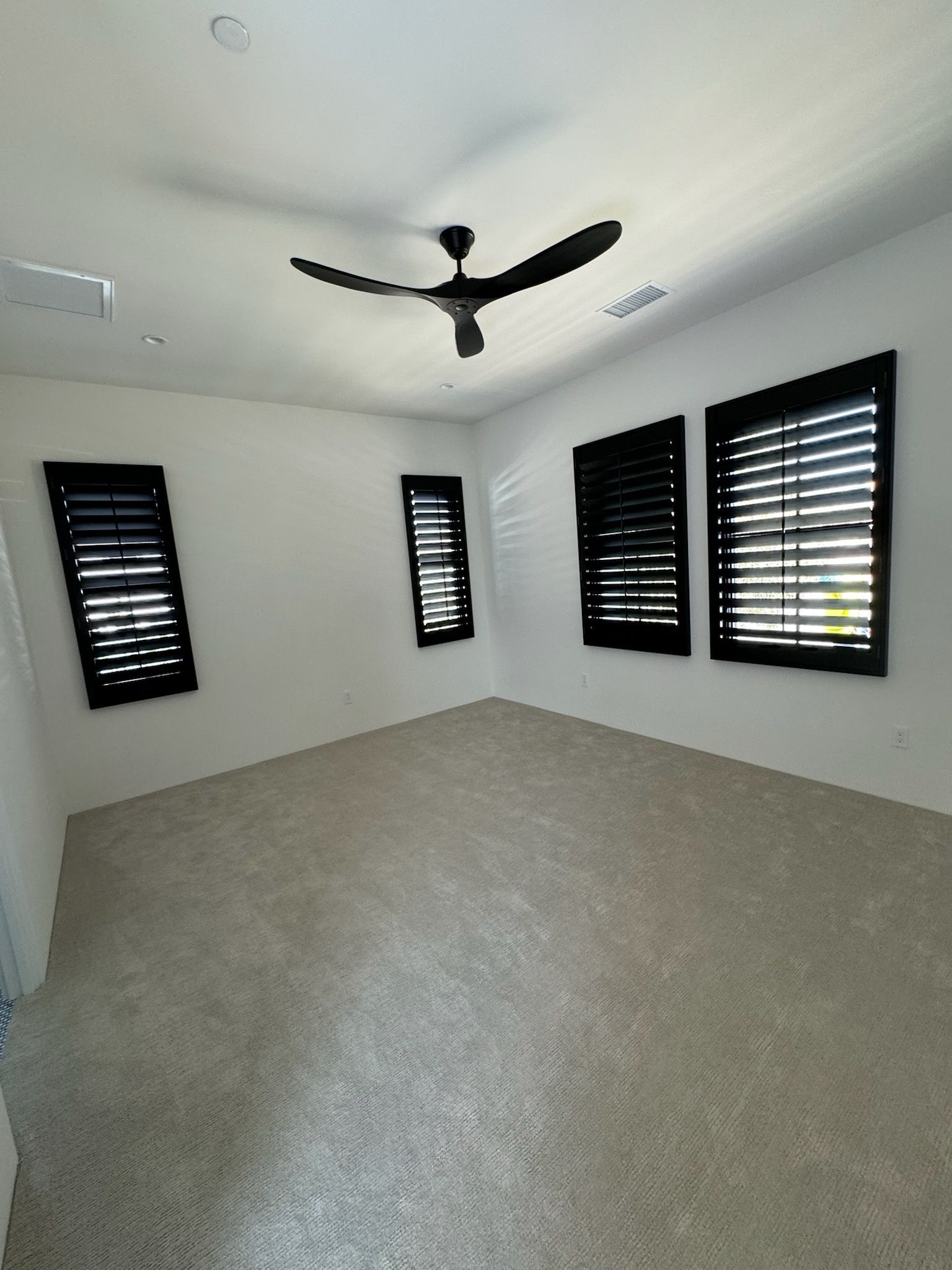 An empty room with a ceiling fan and black shutters on the windows.