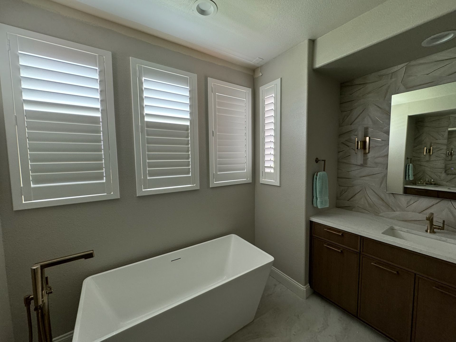 A bathroom with a bathtub, sink, mirror, and shutters.