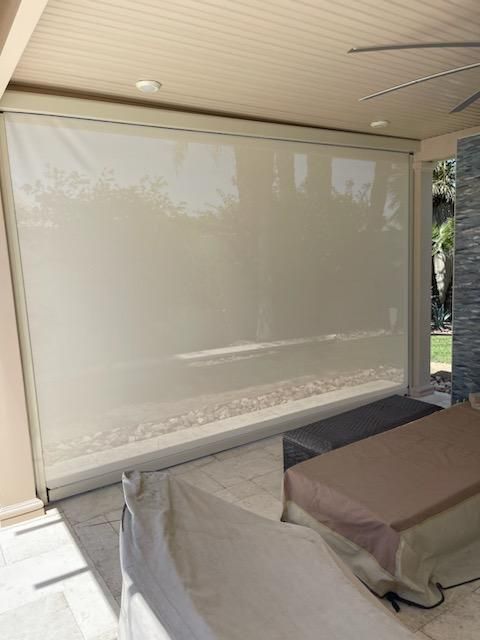 Beige sun shade rolled down on a patio, blocking sunlight.