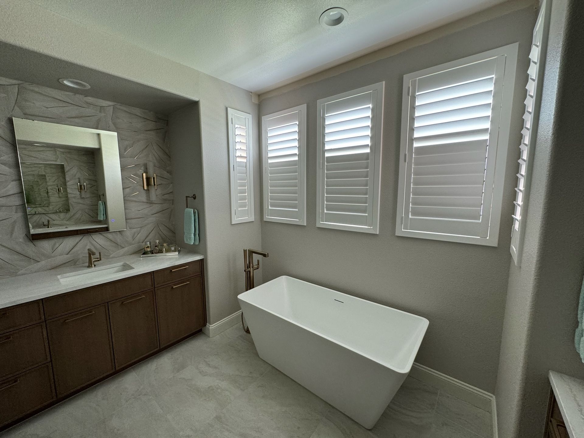A bathroom with a bathtub, sink, mirror, and shutters.