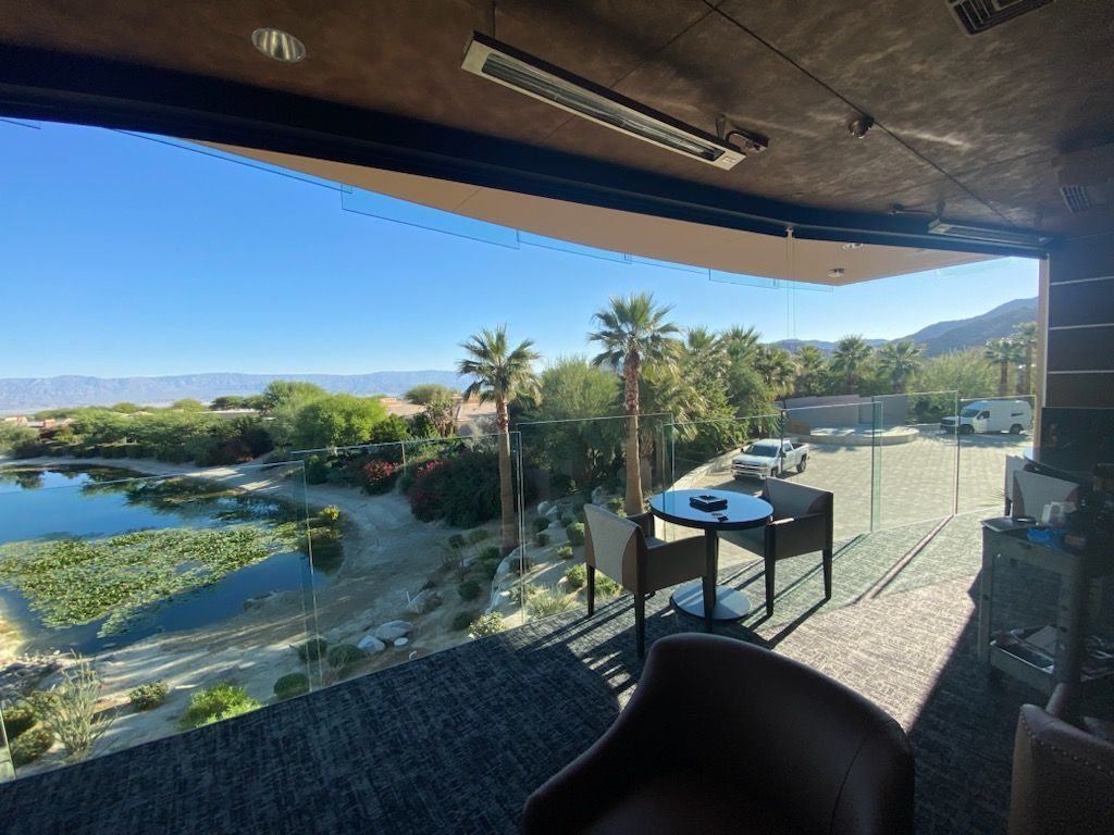 A modern patio overlooking a lake, with a table, chairs, and a sunny landscape.