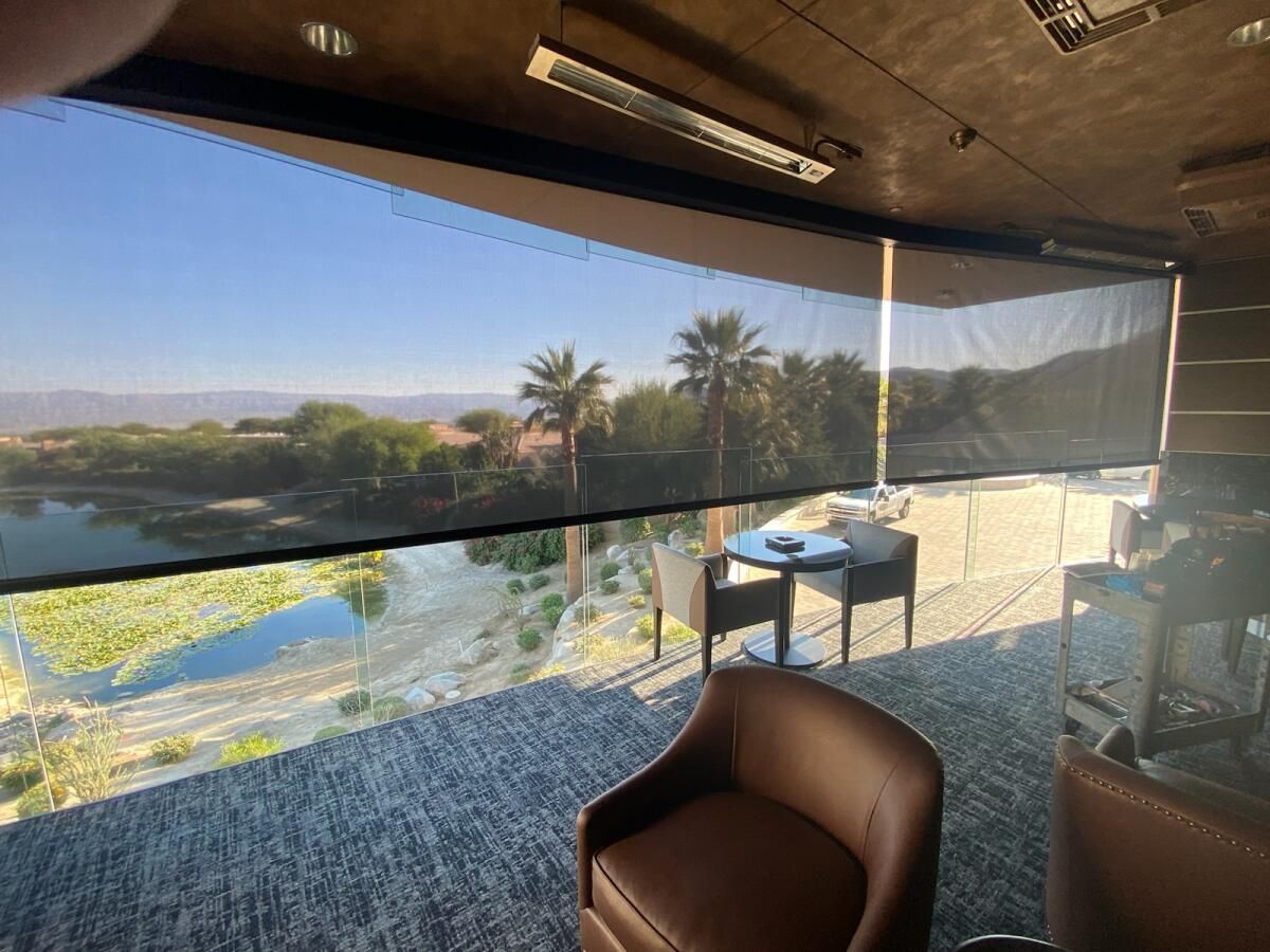 View from a patio with a partially lowered black sun shade, overlooking a scenic landscape with palm trees and a river.