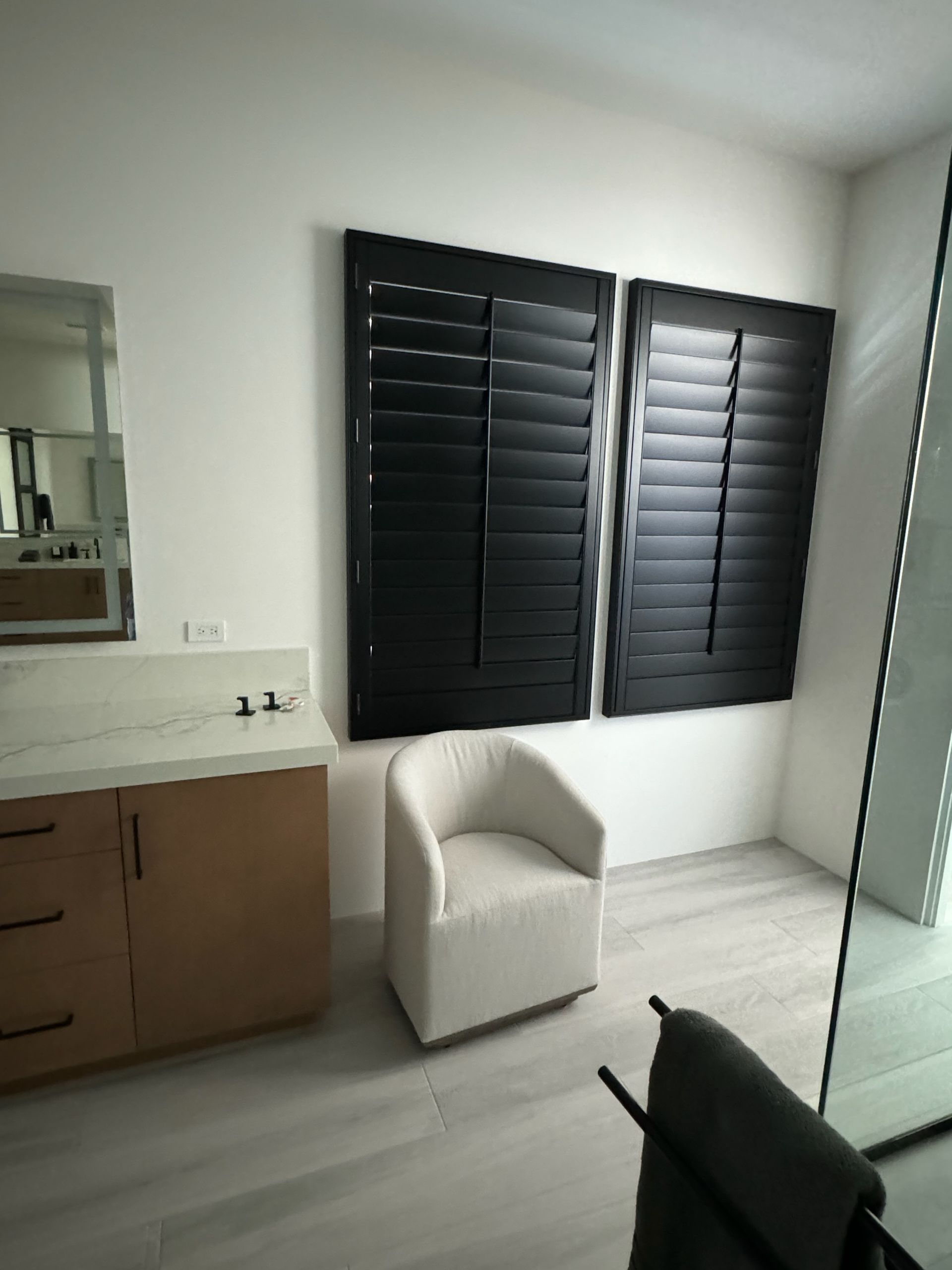 A bathroom with black shutters and a chair