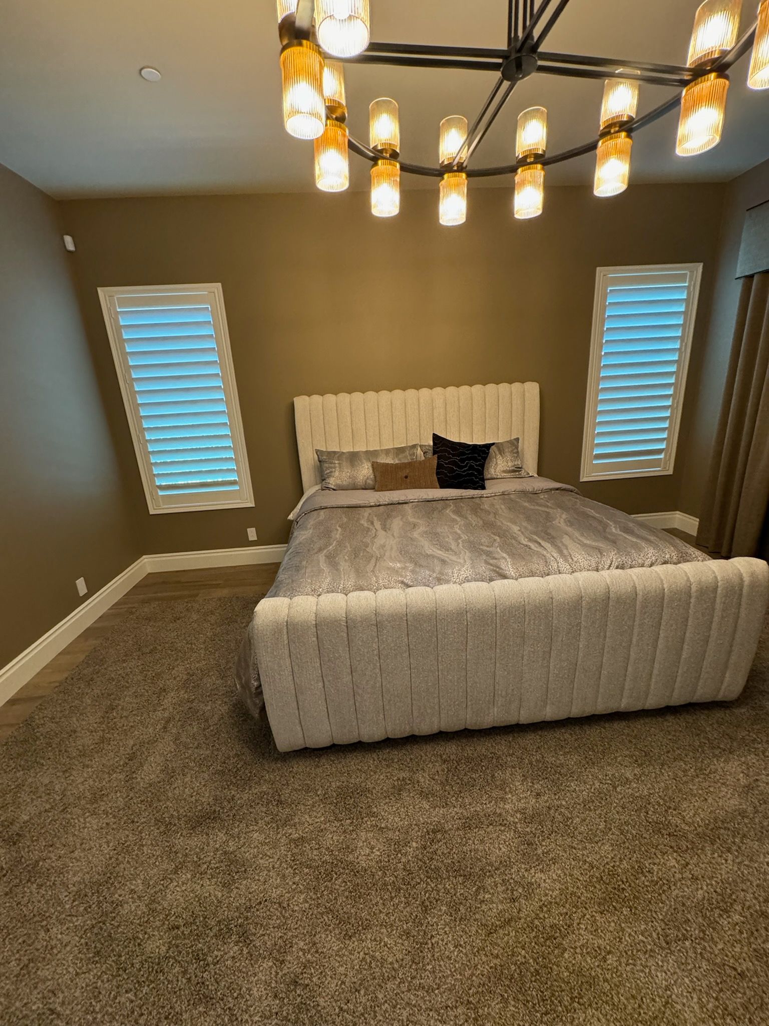 A bedroom with a bed, chandelier, and shutters on the windows.