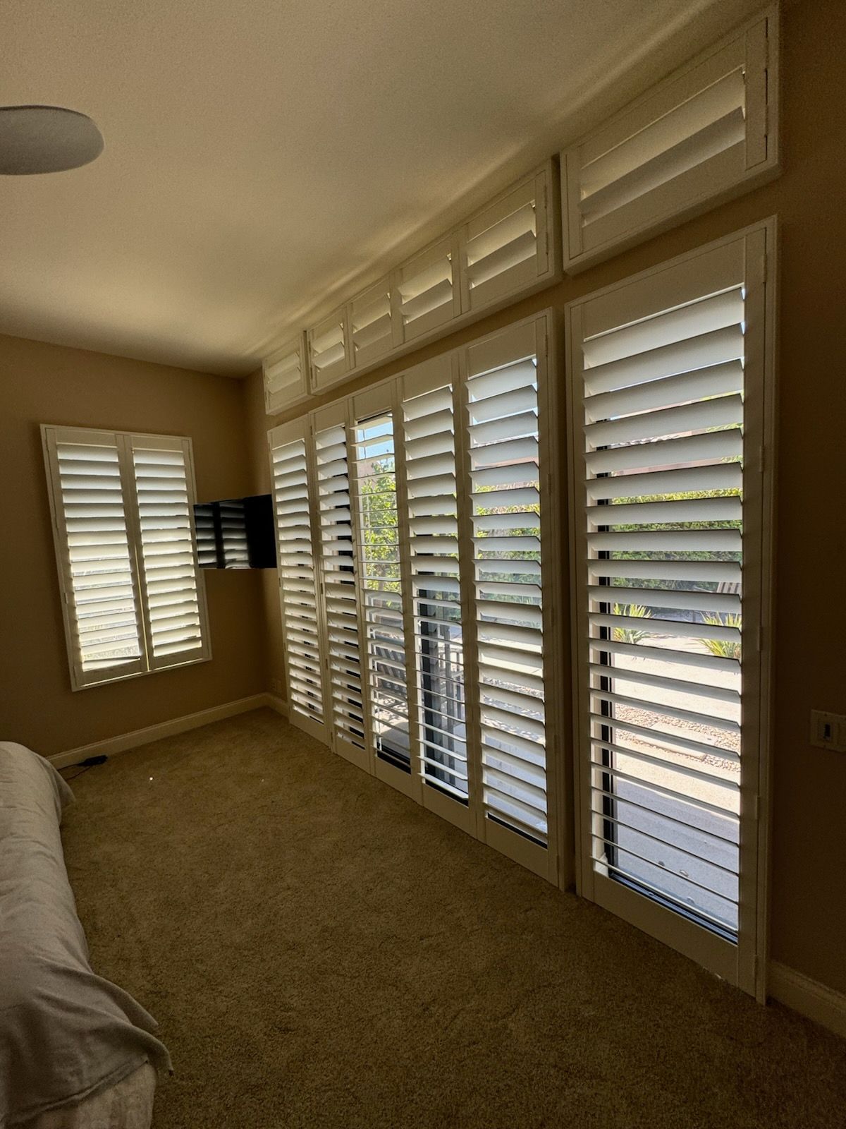A bedroom with a lot of windows and shutters on them.