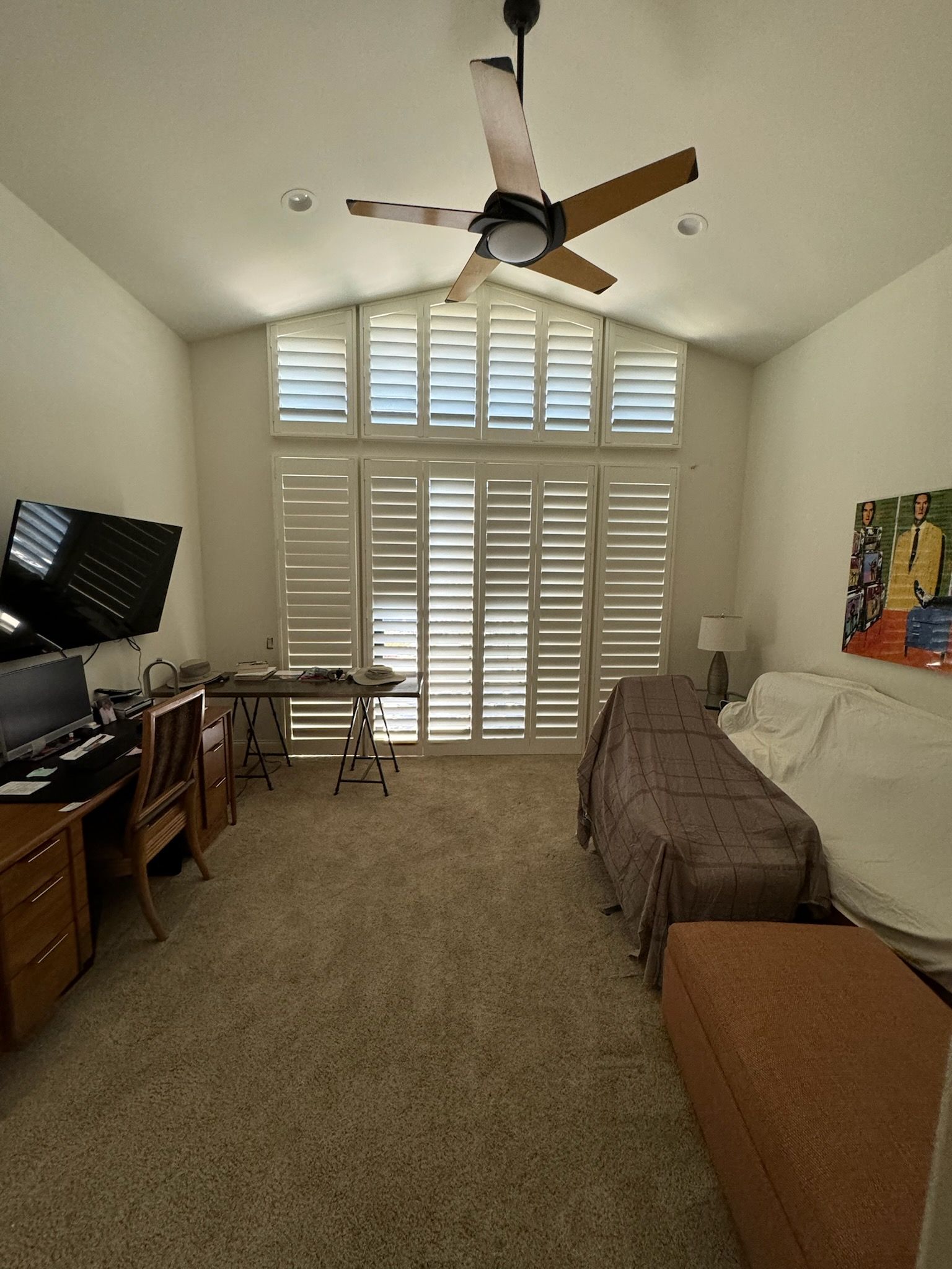 A living room with a ceiling fan and shutters on the windows.