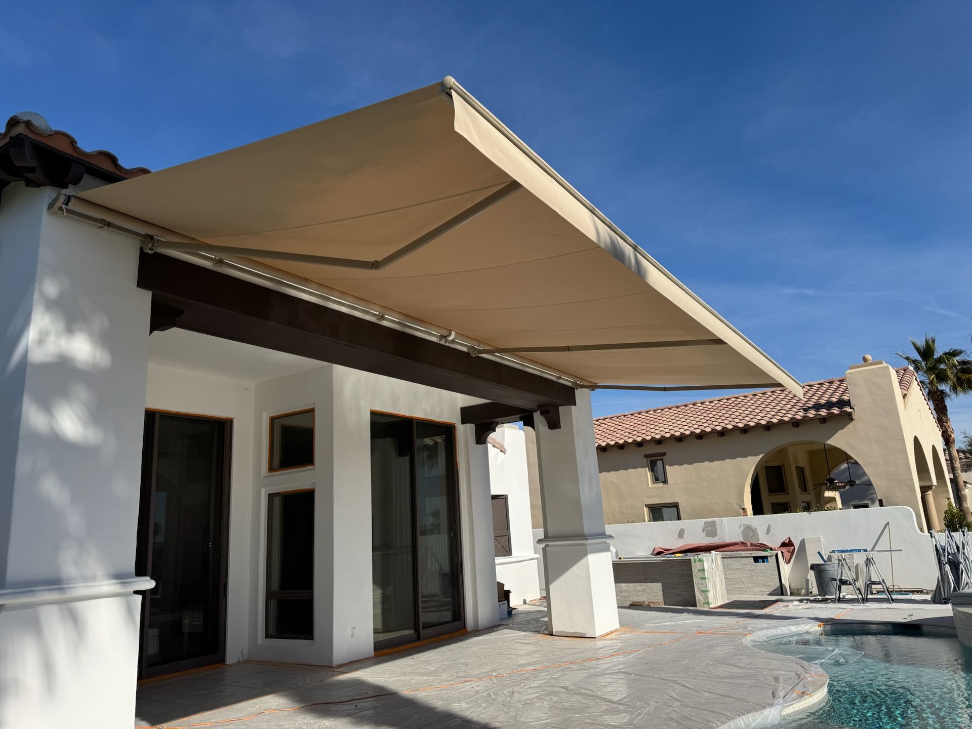 A large awning is covering a patio next to a pool.