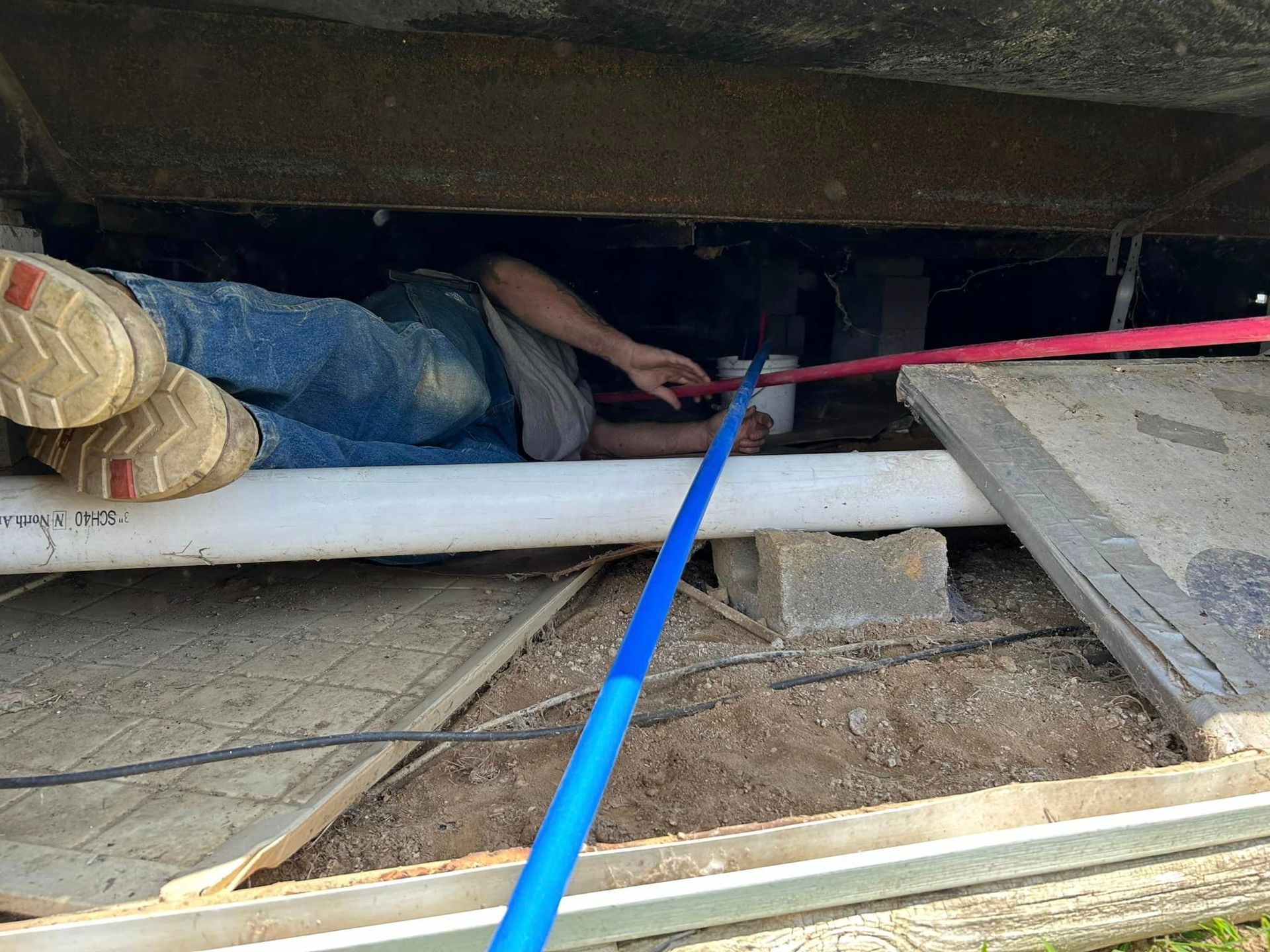 A person is laying under a pipe in a basement.