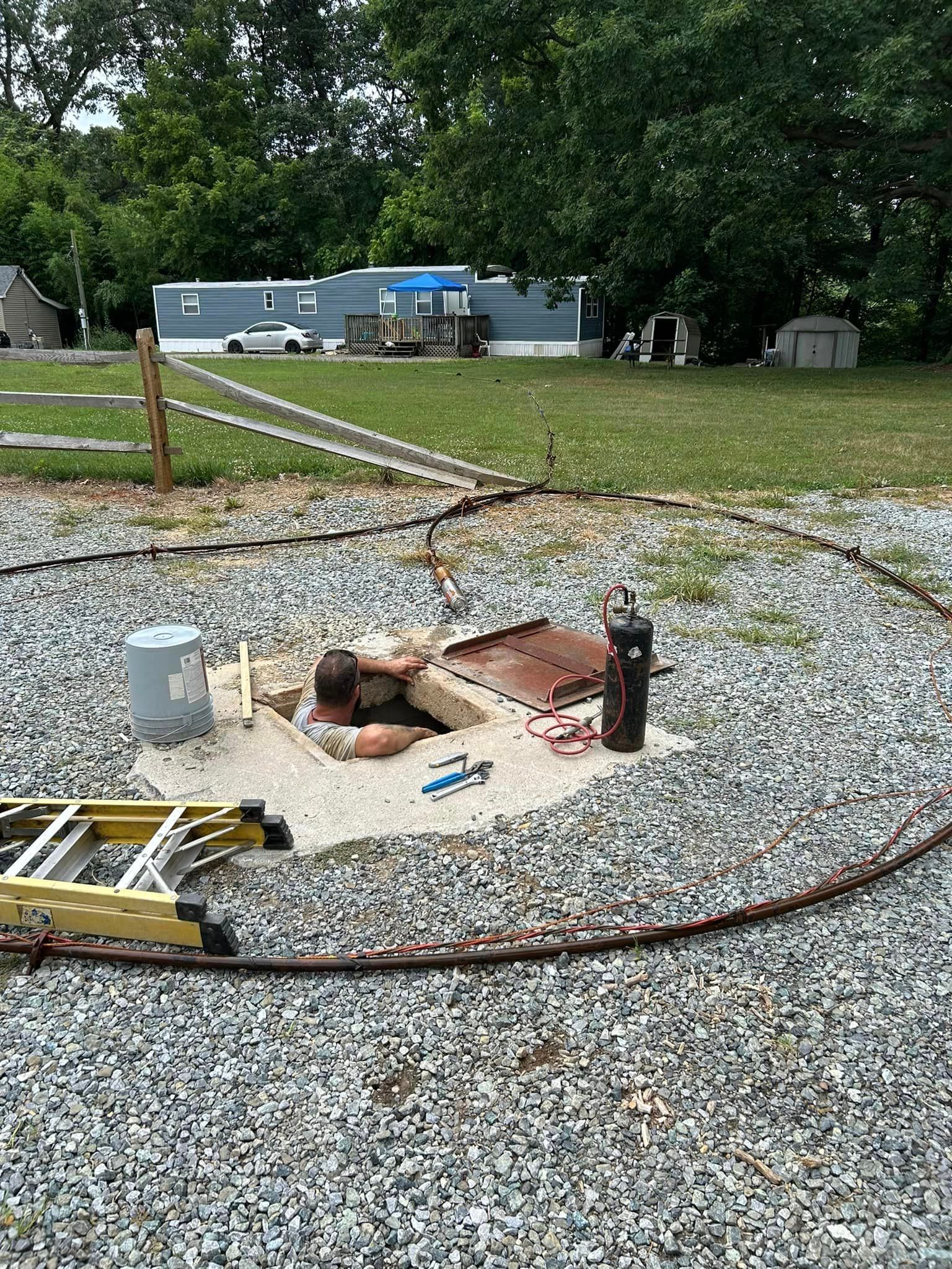 A man is laying in a hole in the ground next to a ladder.