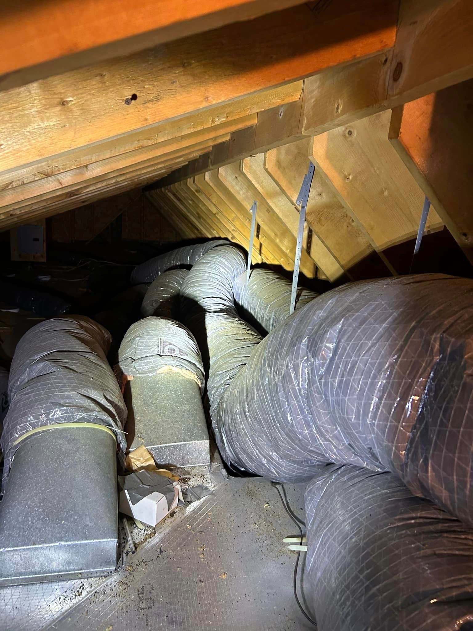 A bunch of ducts are hanging from the ceiling of an attic.