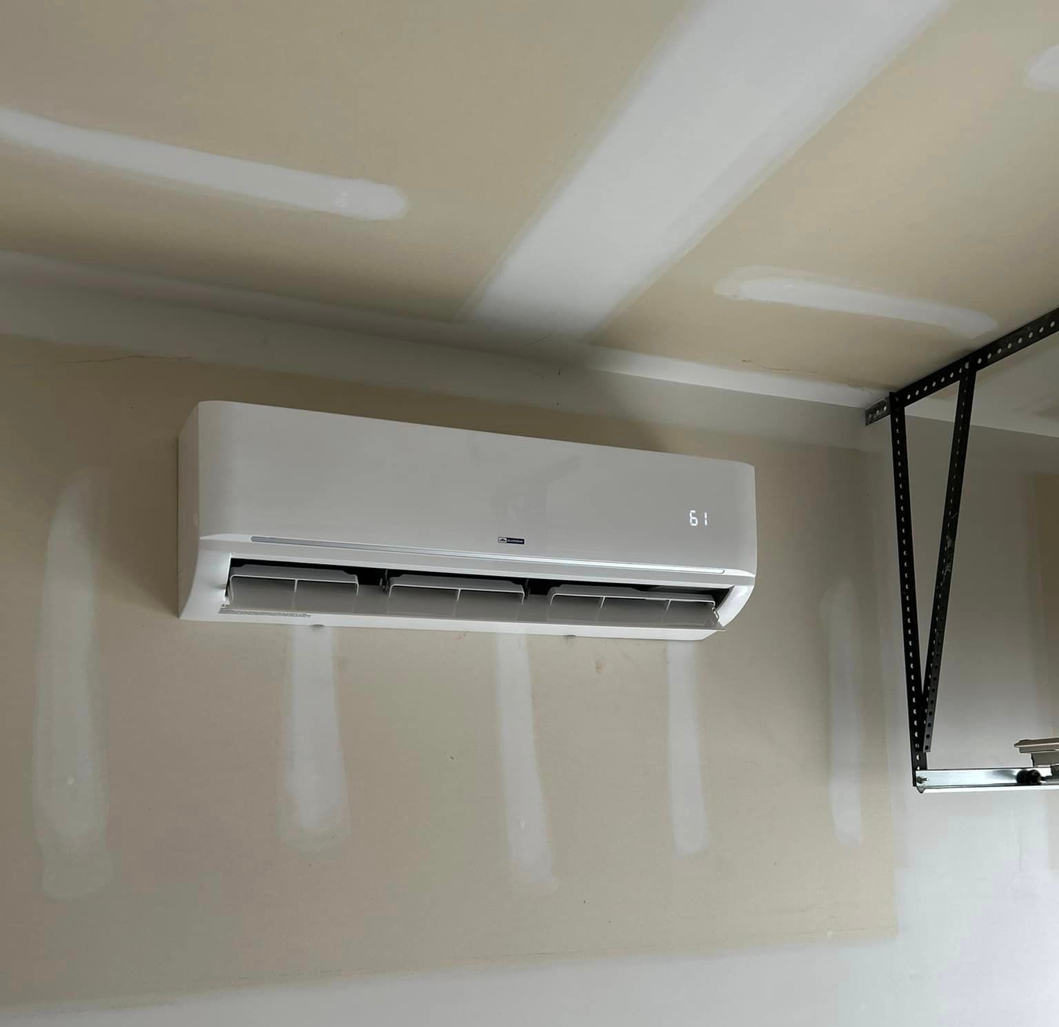 A white air conditioner is hanging from the ceiling in a garage.
