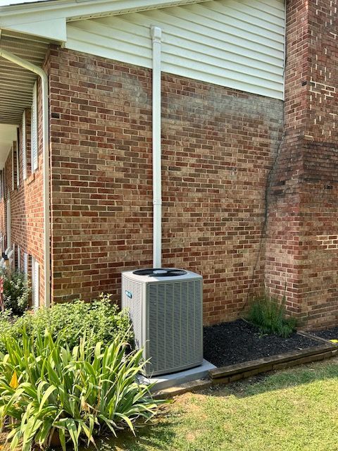 An air conditioner is sitting on the side of a brick house.