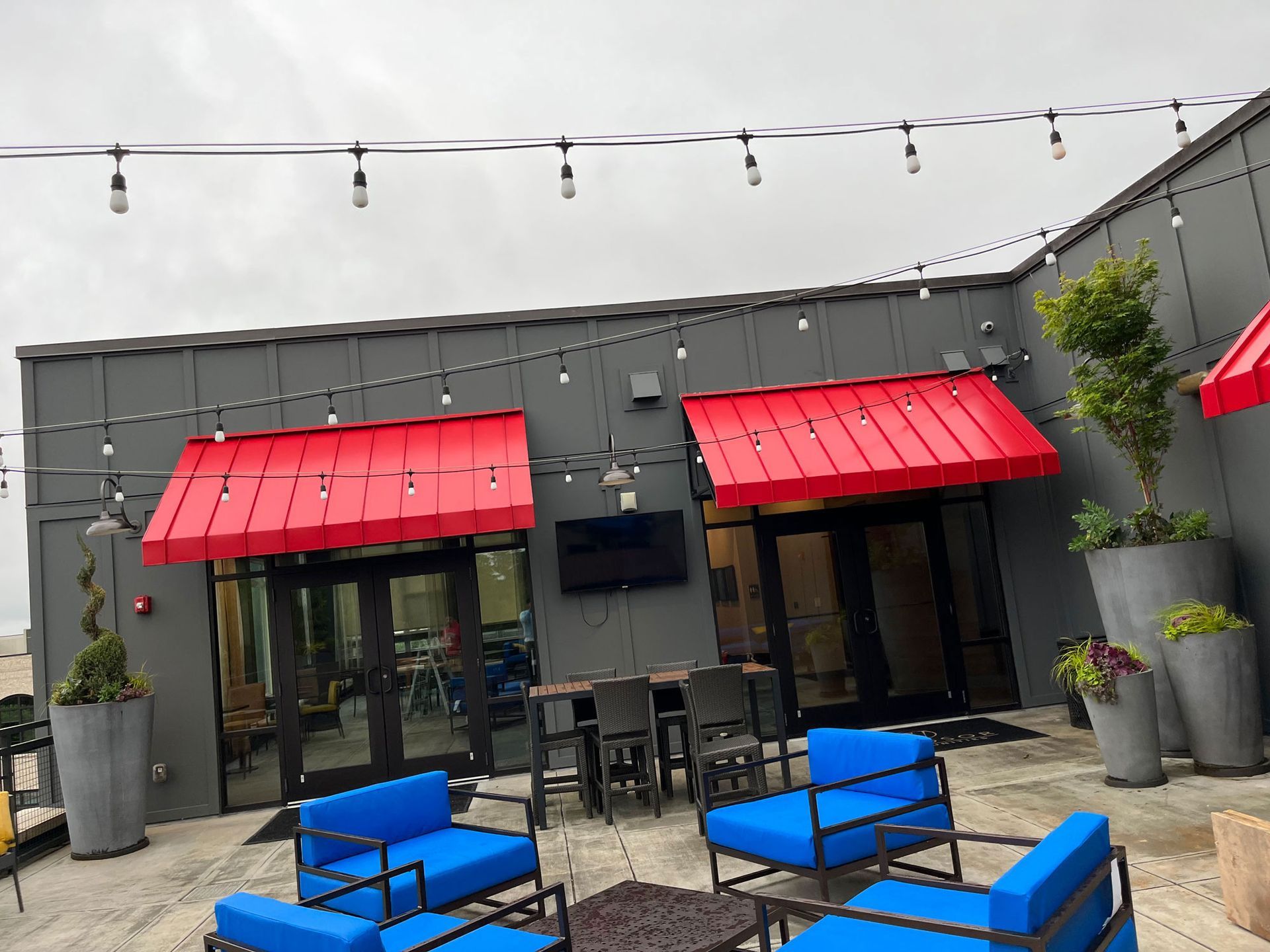 A patio with blue chairs and tables under red awnings.