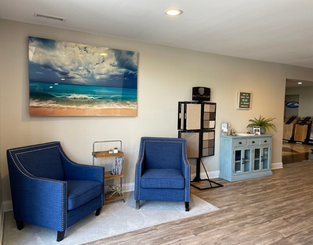 A living room with two blue chairs and a painting on the wall.