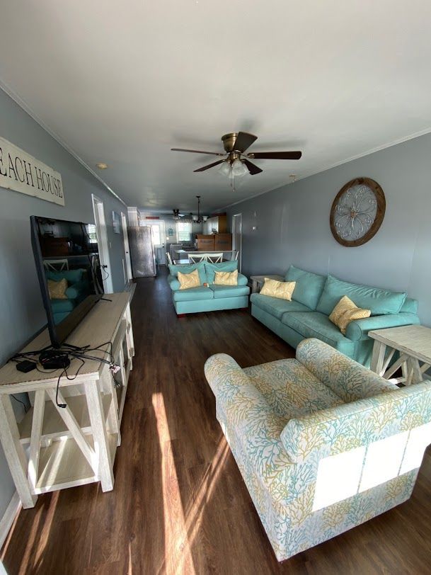 A living room with a couch , chair , television and ceiling fan.