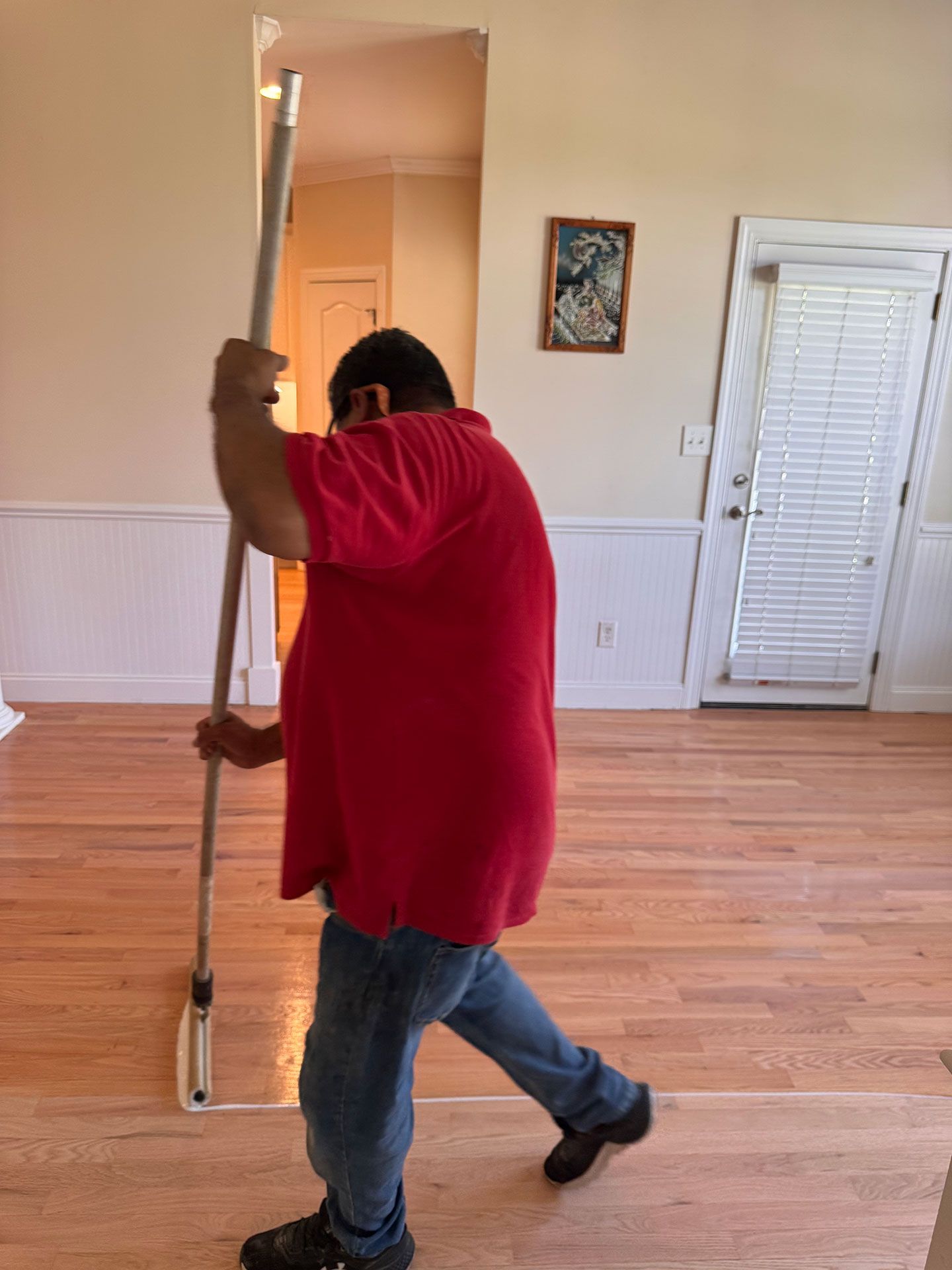 A man in a red shirt is holding a mop in a living room.