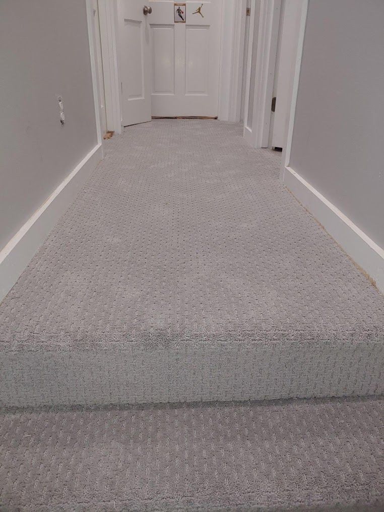 A hallway with a carpeted floor and stairs leading to a door.