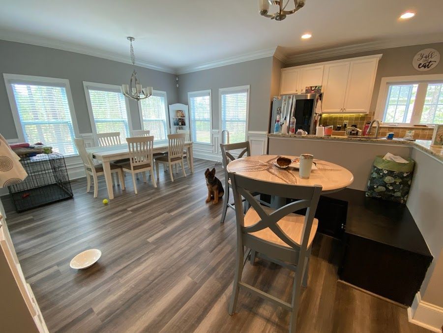 A dog is standing in a living room next to a table and chairs.