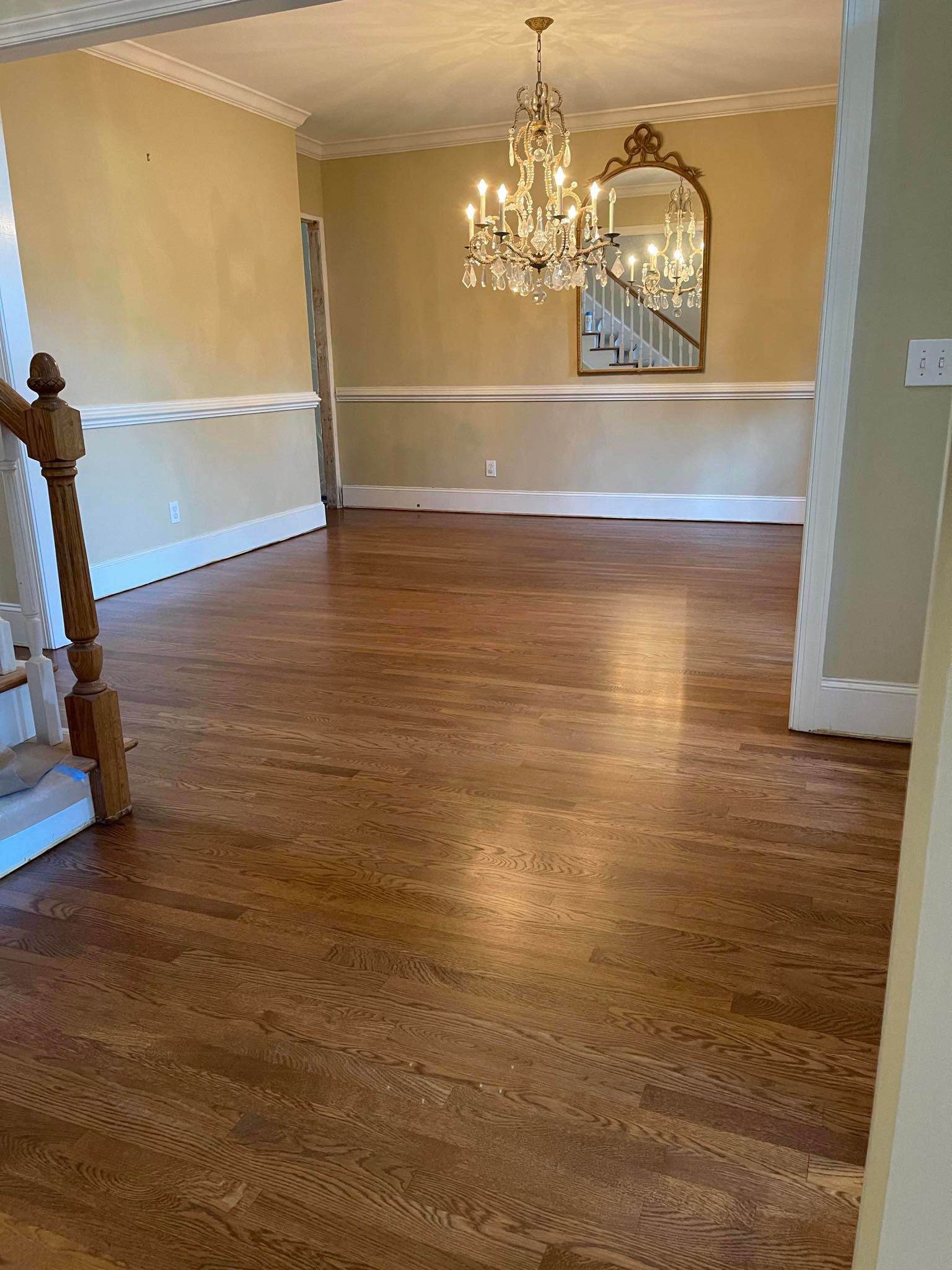 An empty dining room with hardwood floors and a chandelier hanging from the ceiling.