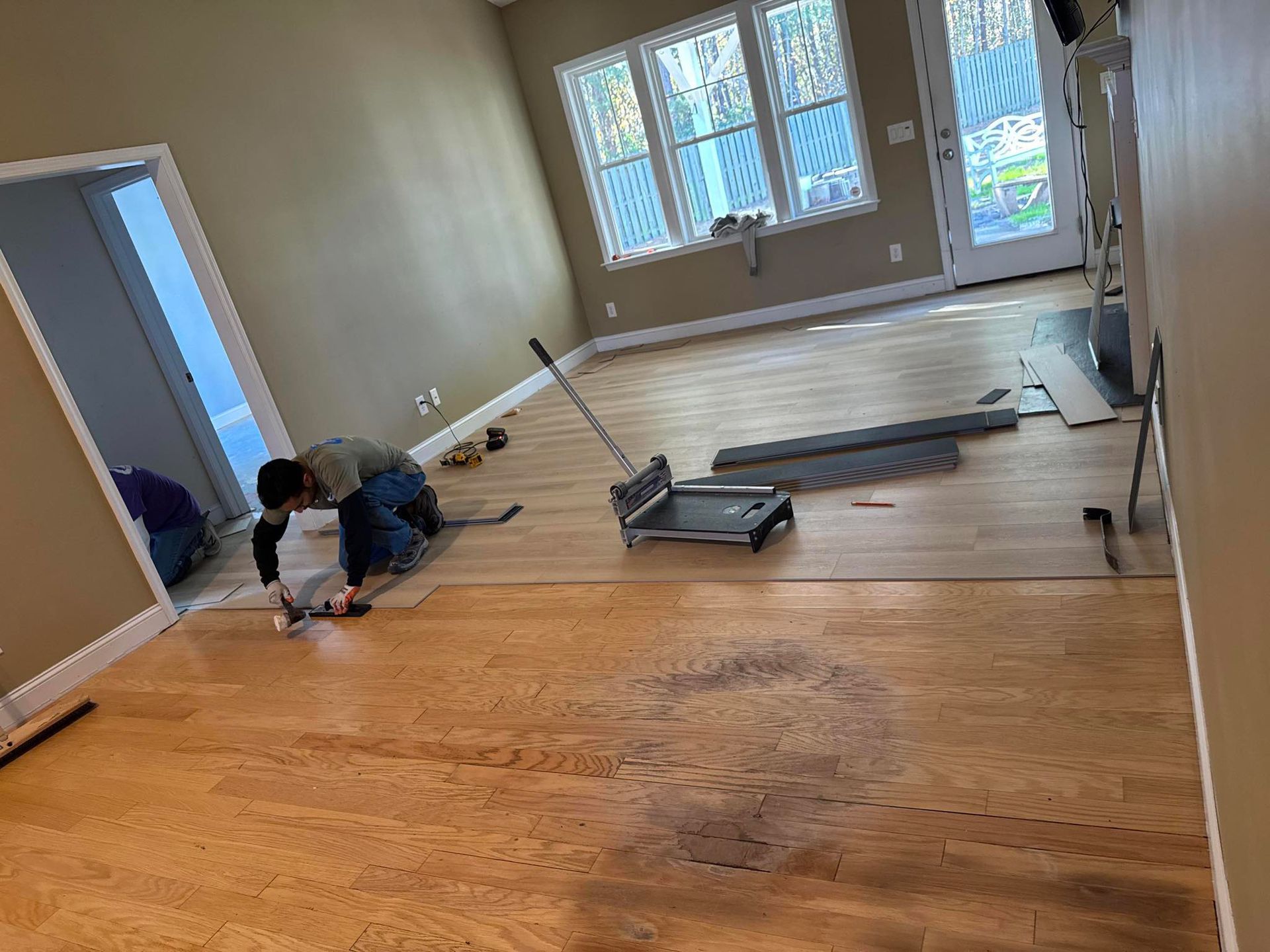 A person is laying wooden flooring in a living room.