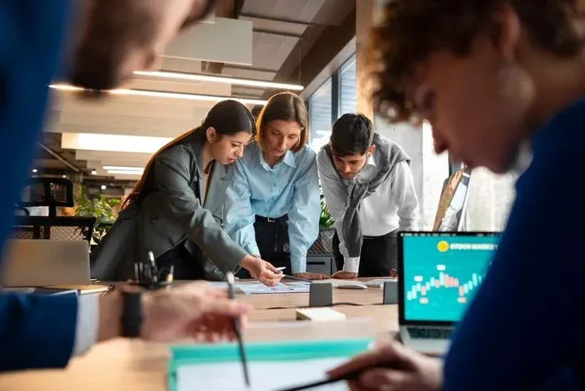 Colleagues leaning over a table, discussing documents in a bright office meeting room