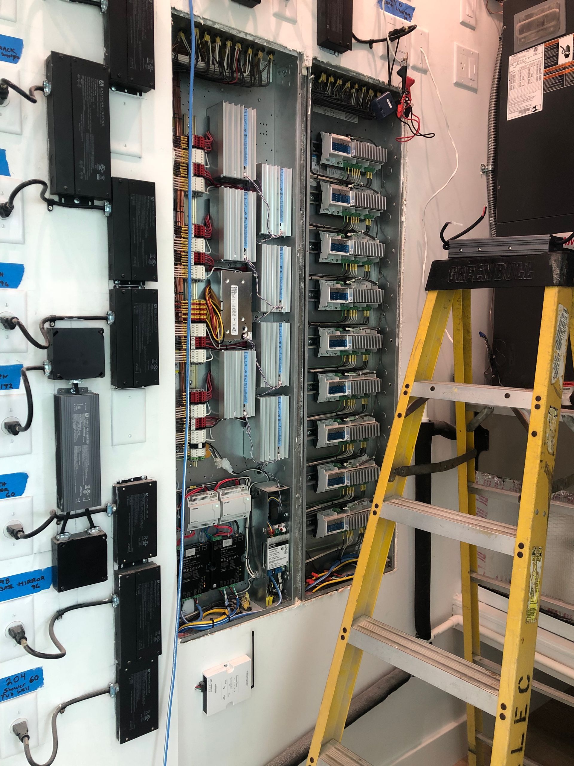 A yellow ladder is sitting in front of a wall filled with electrical equipment.