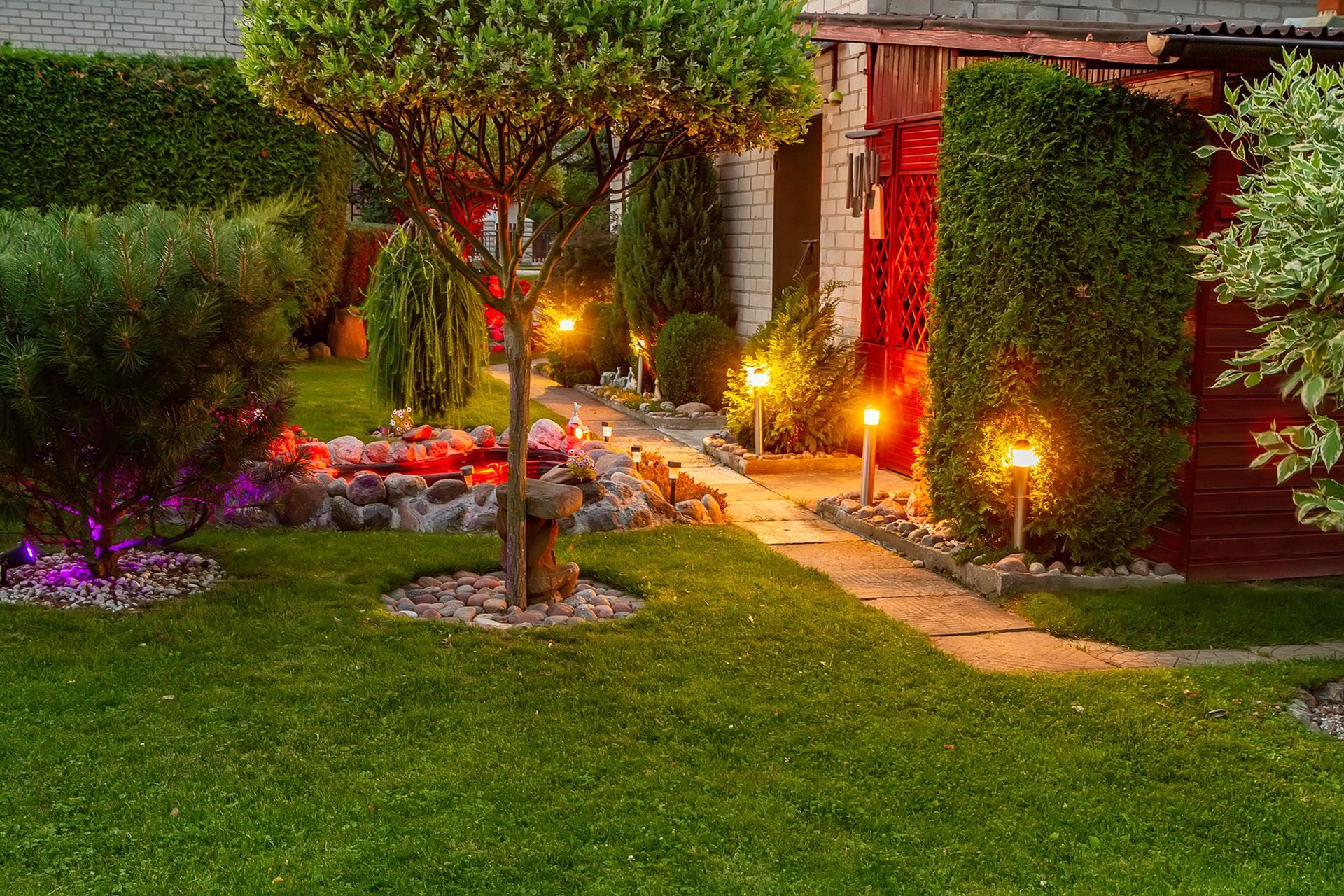 A lush green garden with a path leading to a house at night.